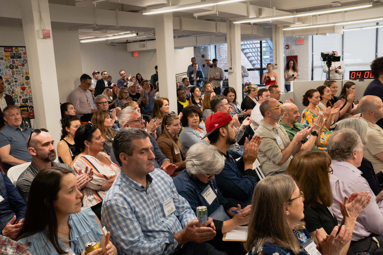 Rows of seated attendees clapping, several holding drinks, with a countdown clock visible at the back.