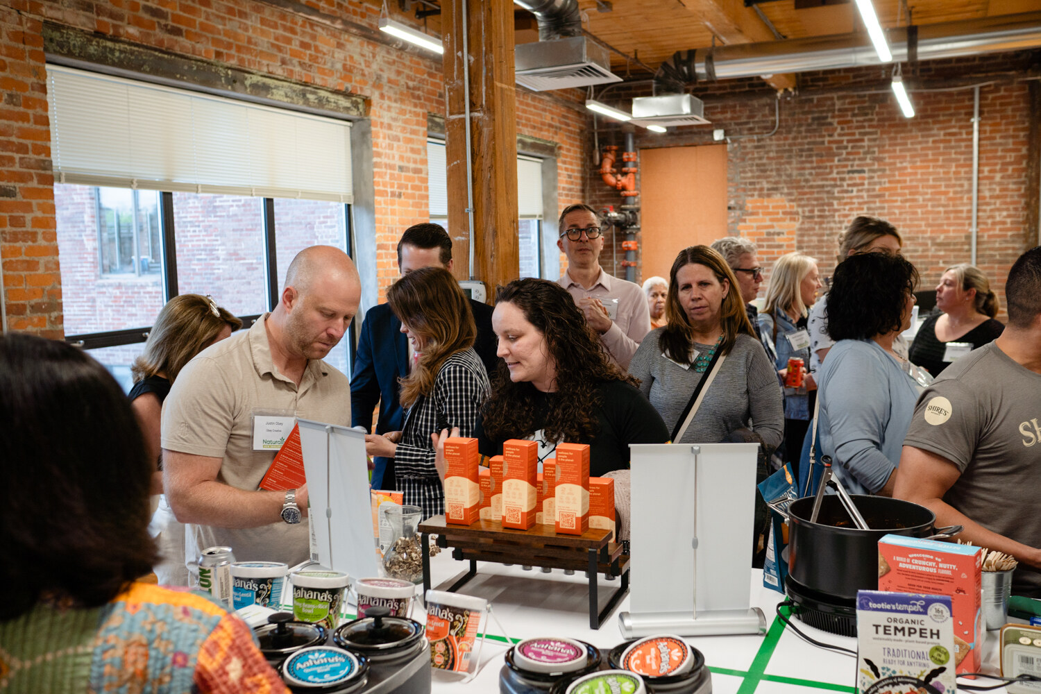 Attendees gather around a table with slow cookers, small tubs and packages of organic tempeh.