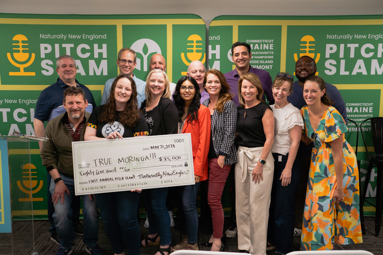 A large group of smiling people stands in front of the Pitch Slam backdrop holding an oversized check.