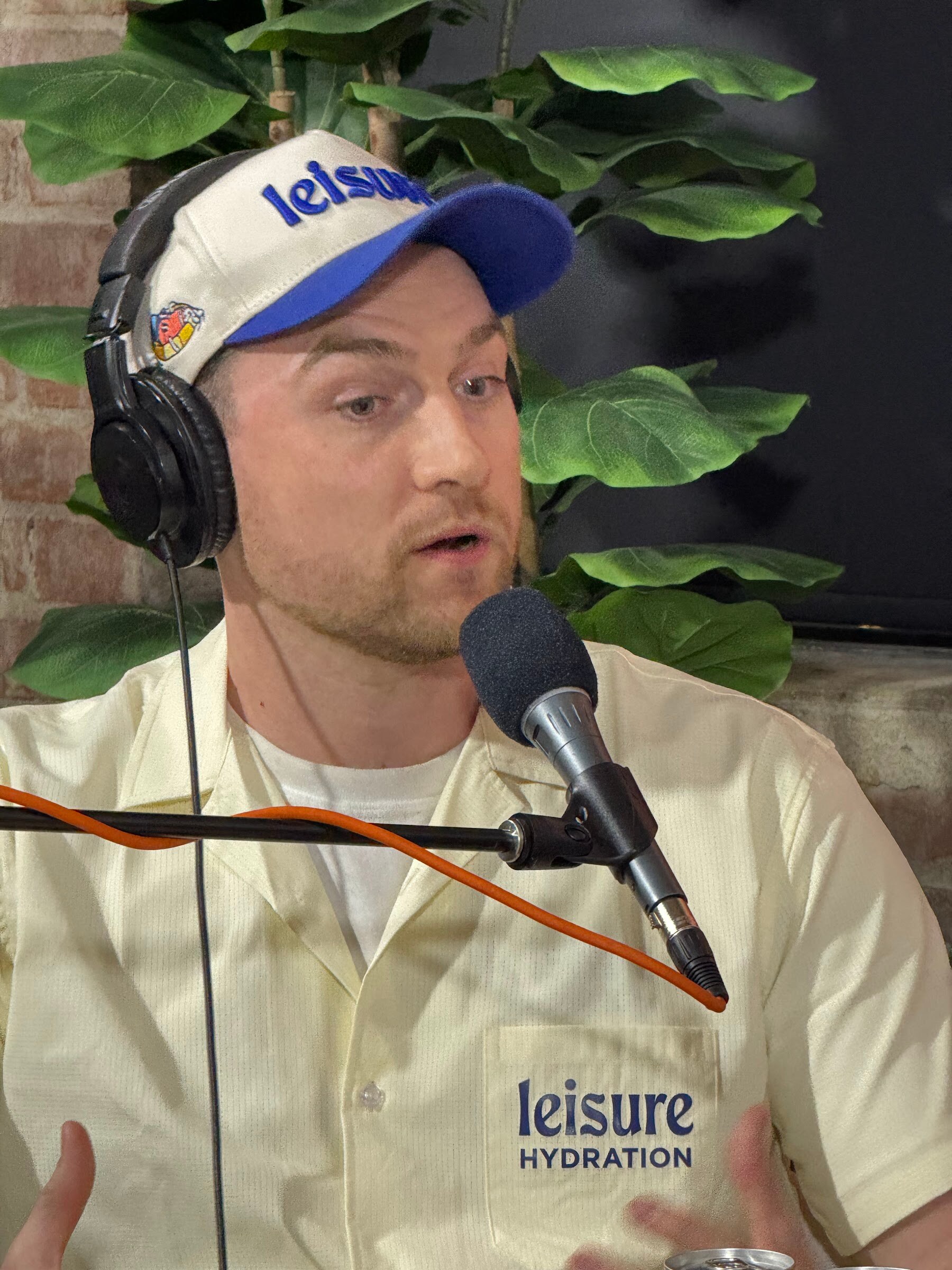 Man in a Leisure cap and headphones speaking into a microphone.