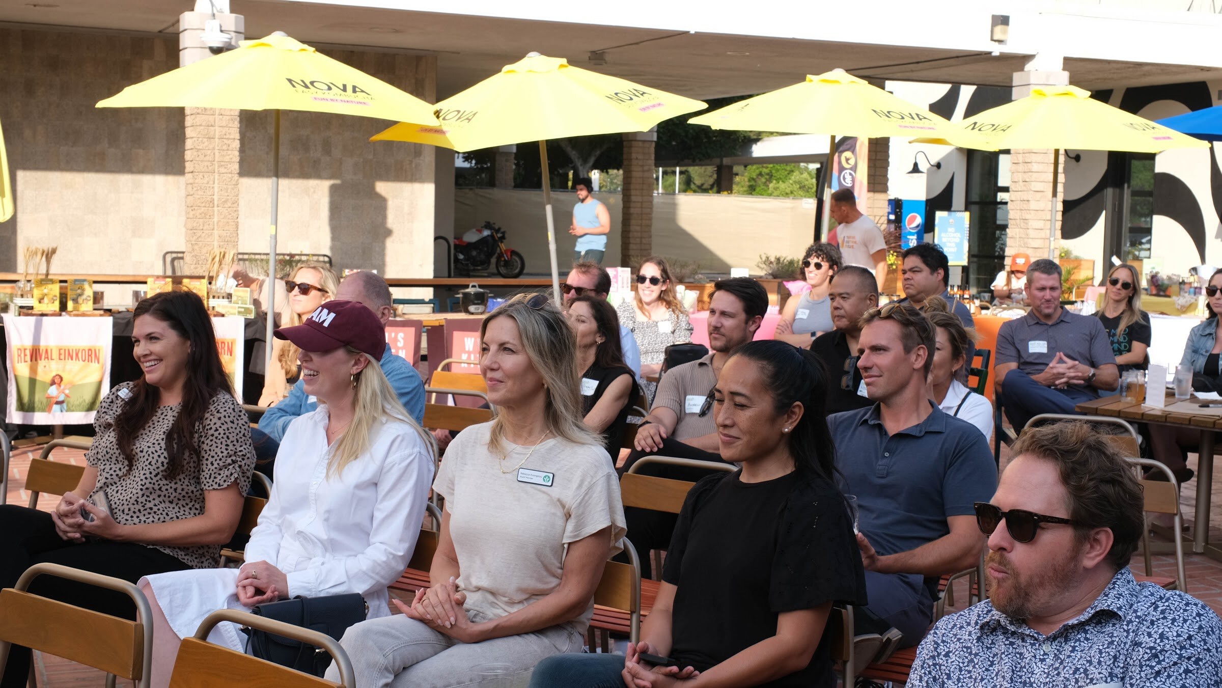 Rows of seated guests with name tags looking toward the stage, with yellow umbrellas behind them.