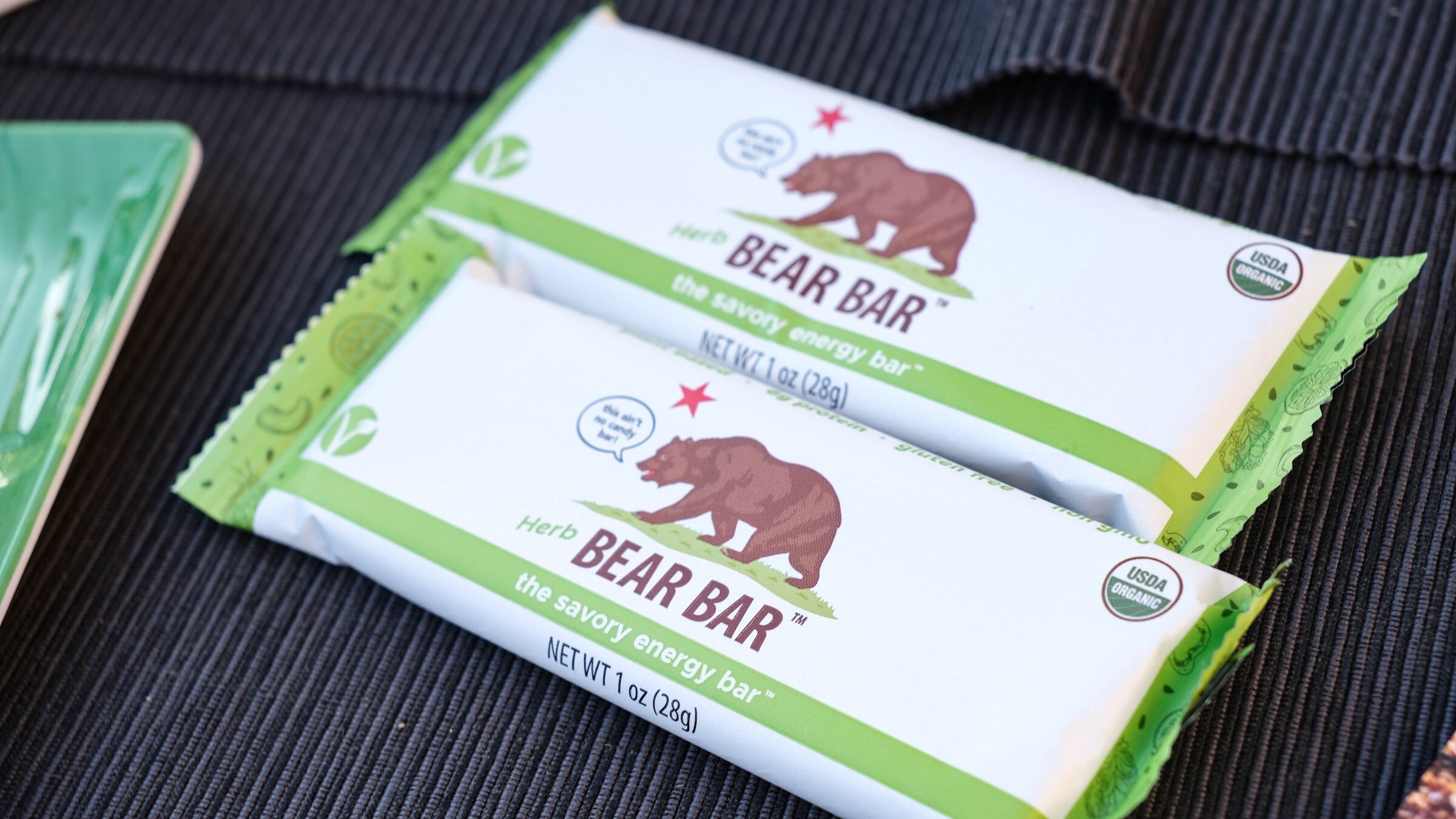 Two green and white Bear Bar packages with a bear logo on a dark placemat.