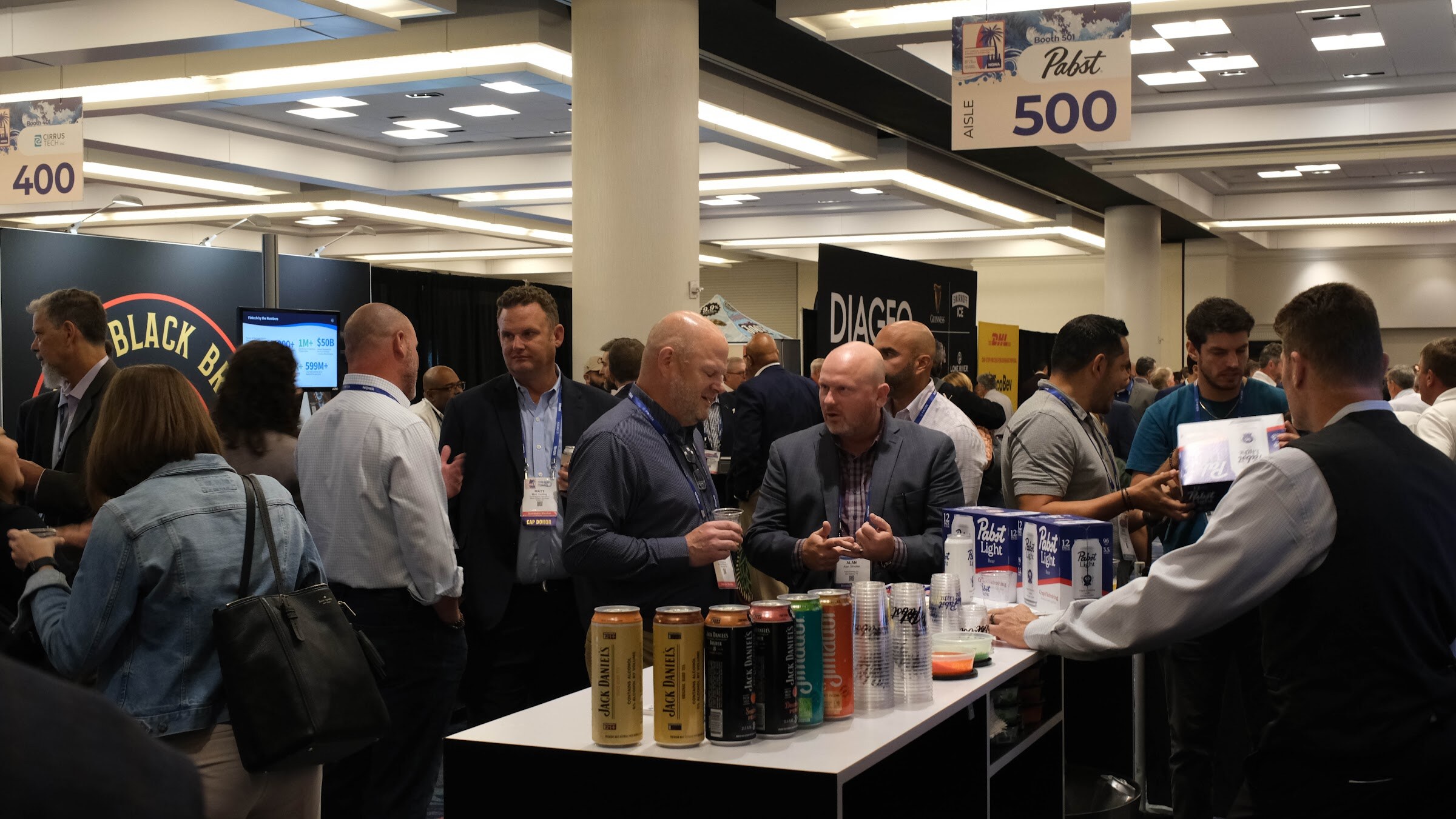 Group of attendees gathered at a booth with cans on a white counter beneath a Pabst aisle sign.