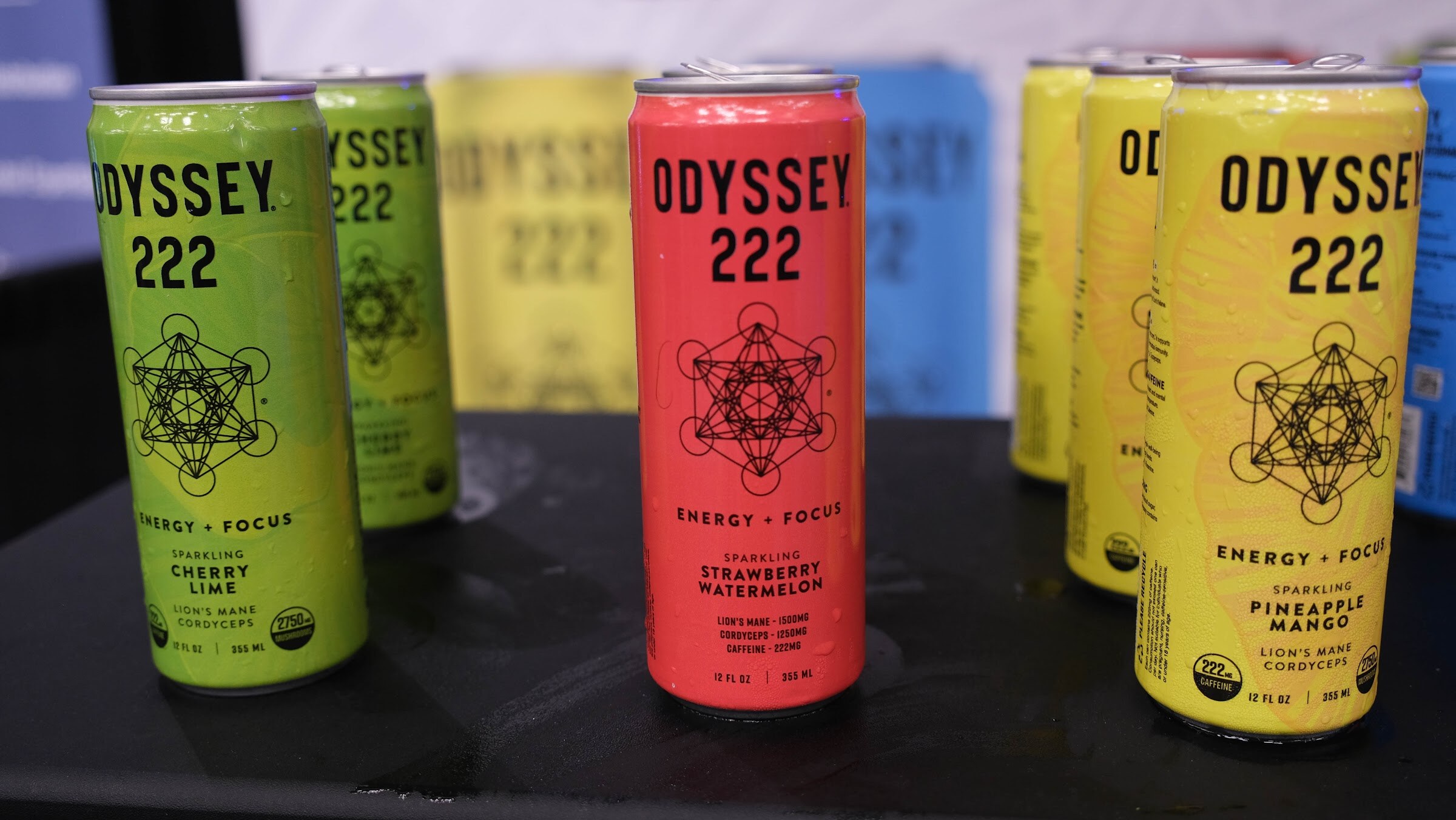Three cans of Odyssey 222 in green, red and yellow on a black table.