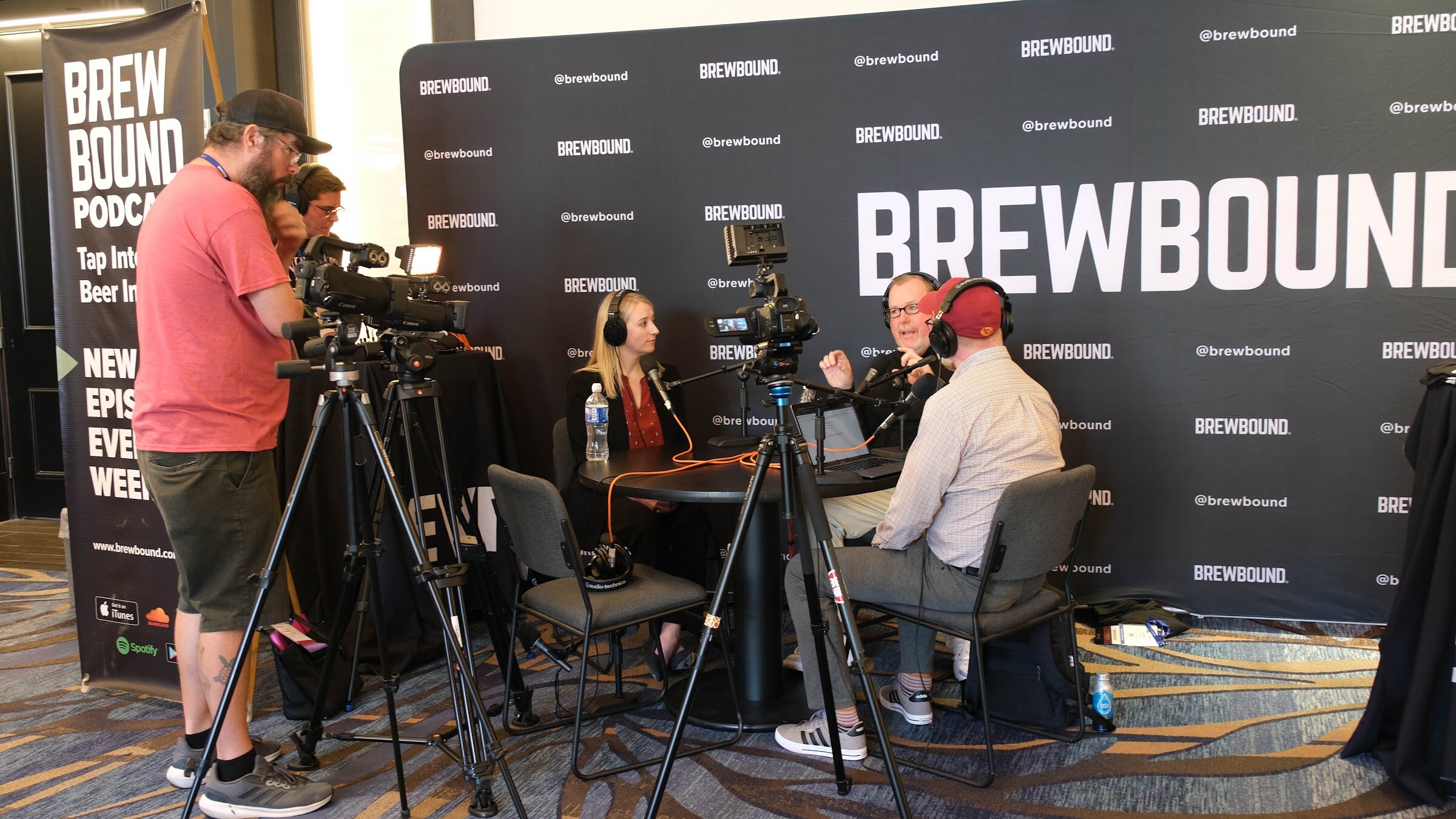 Brewbound-branded backdrop with a camera operator and two people recording an interview at a round black table.