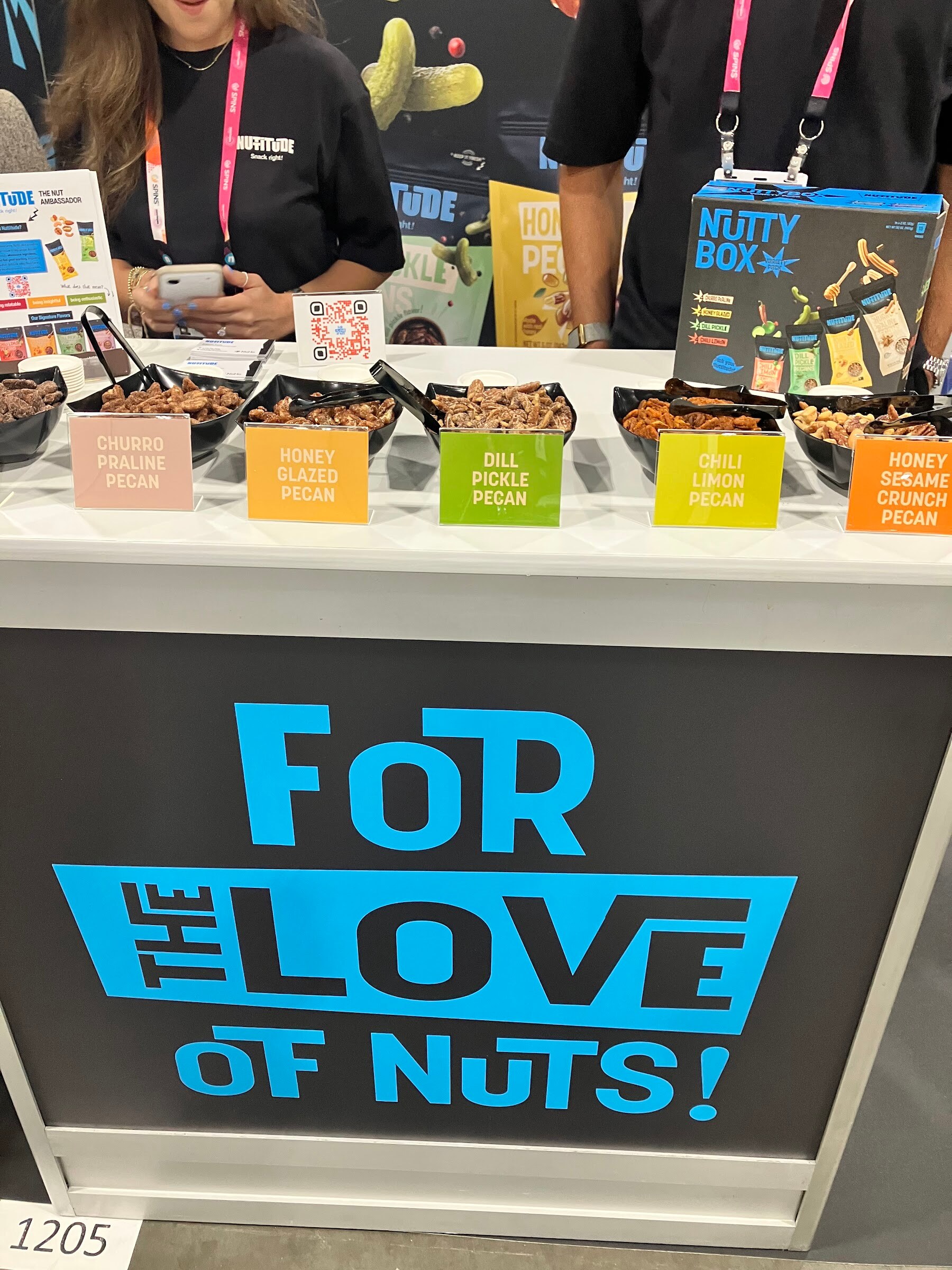 Sample trays of flavored pecans labeled Honey Glazed and Dill Pickle above a blue For the Love of Nuts sign.