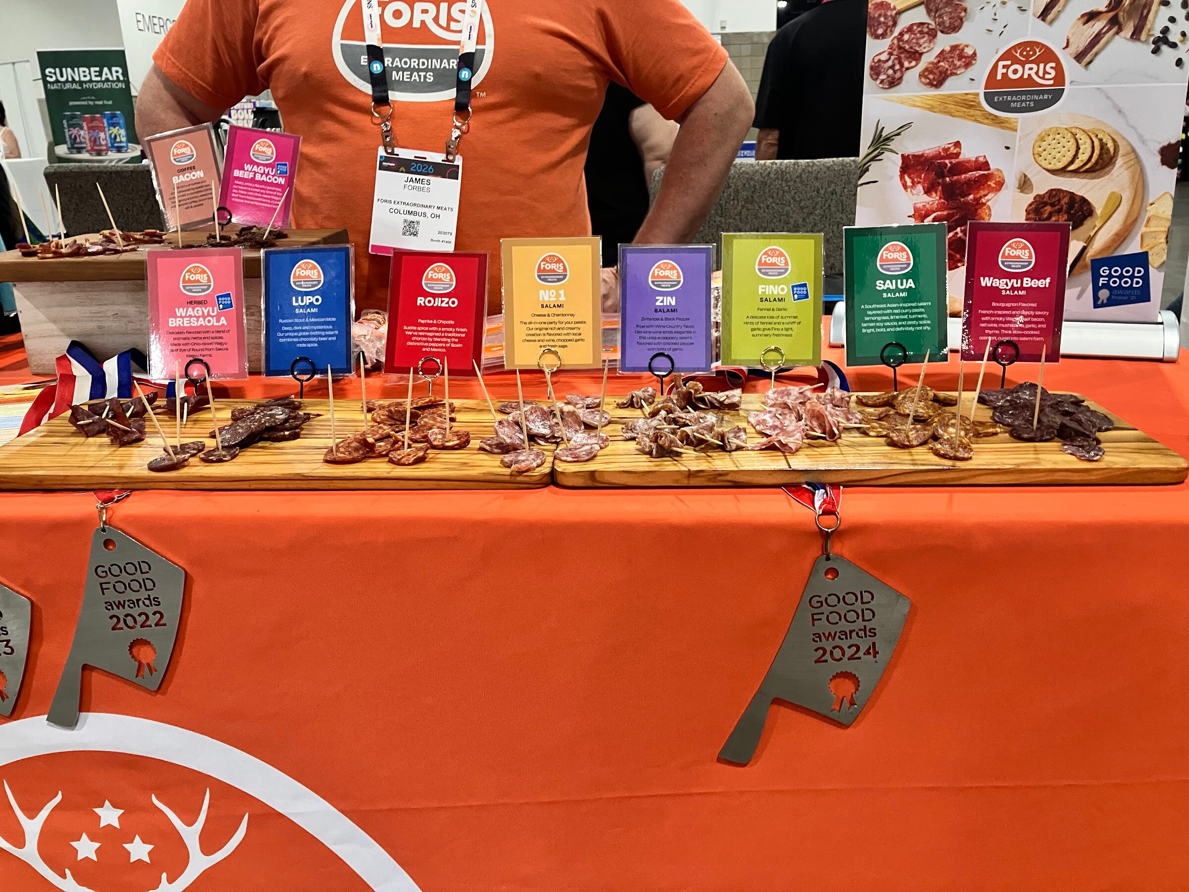 Charcuterie samples on wooden boards behind colorful flavor cards on an orange Foris Extraordinary Meats table.