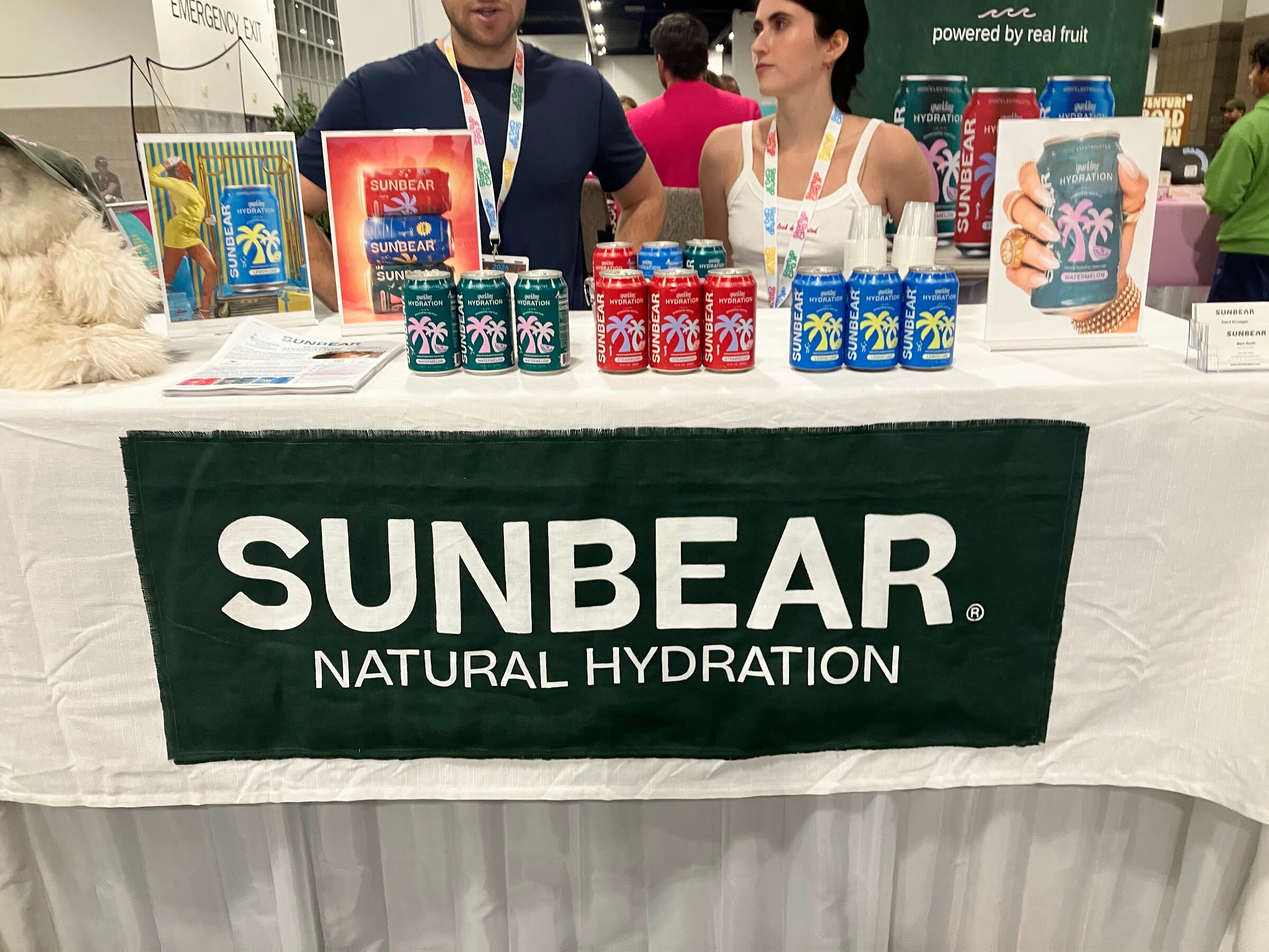 Cans of Sunbear drinks on a table above a green Sunbear Natural Hydration banner.