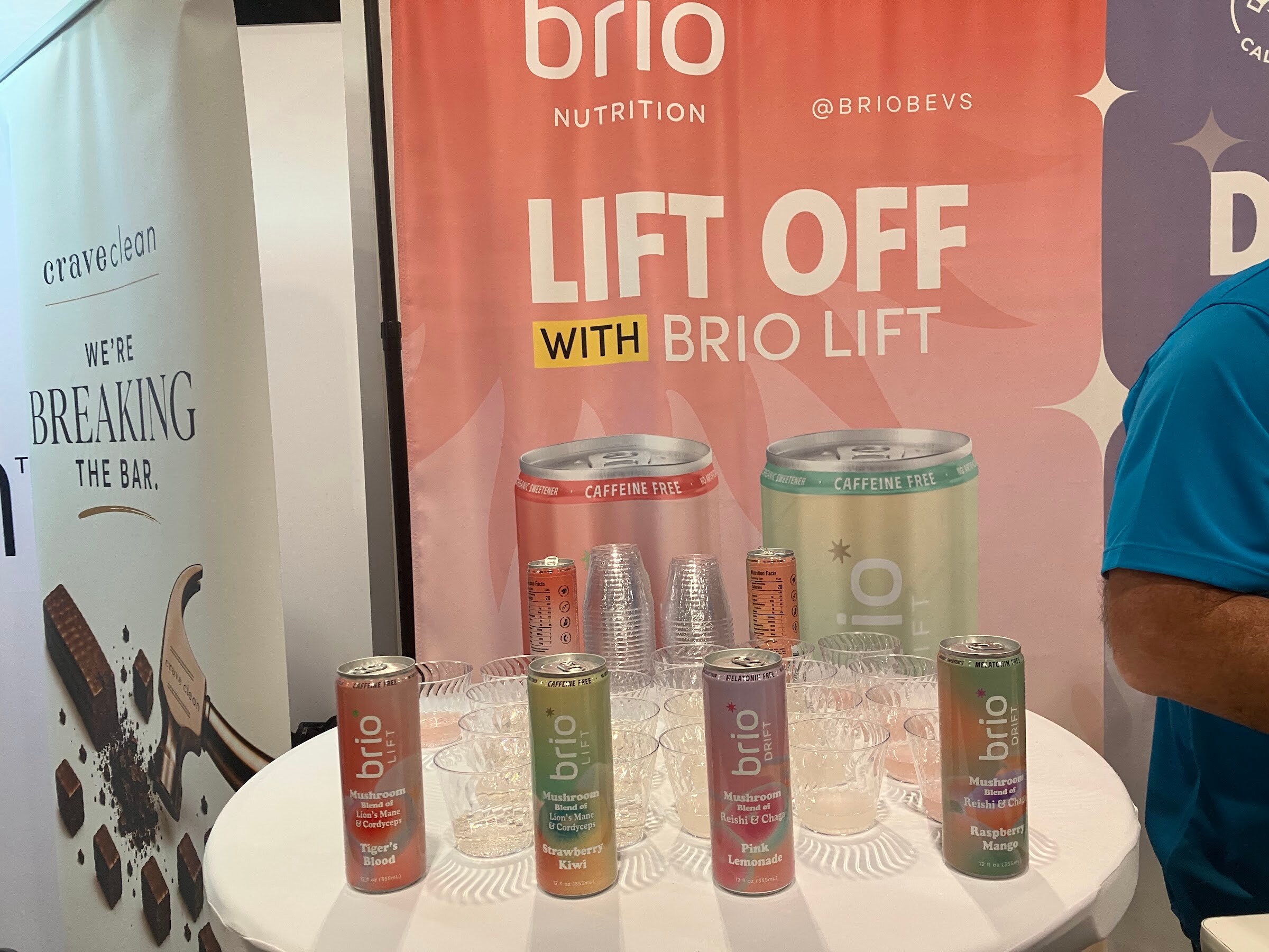 Cans of Brio Lift on a white table in front of a pink sign reading Lift off with Brio Lift.