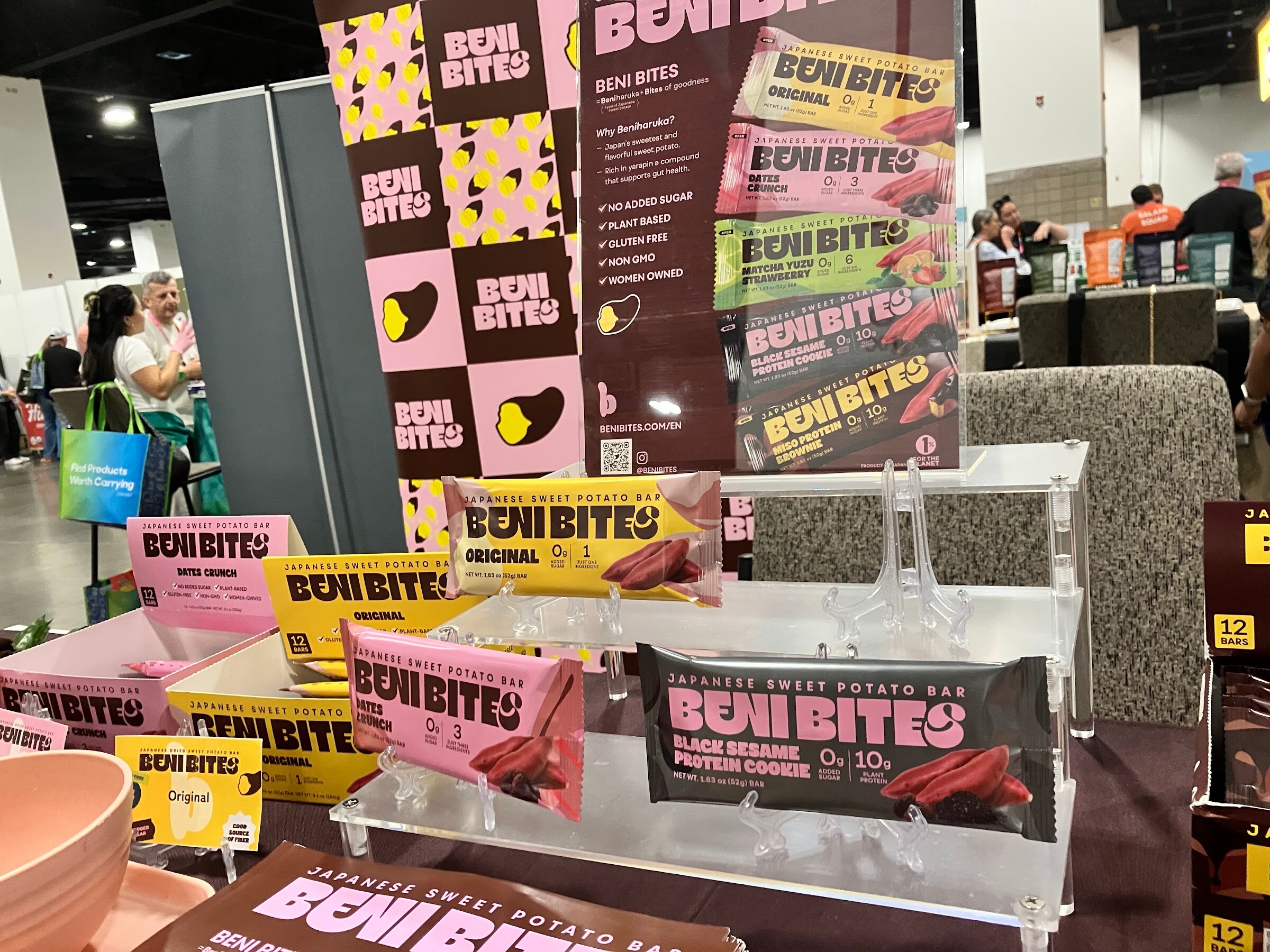 Beni Bites sweet potato bars on acrylic stands in front of a pink and yellow Beni Bites display.