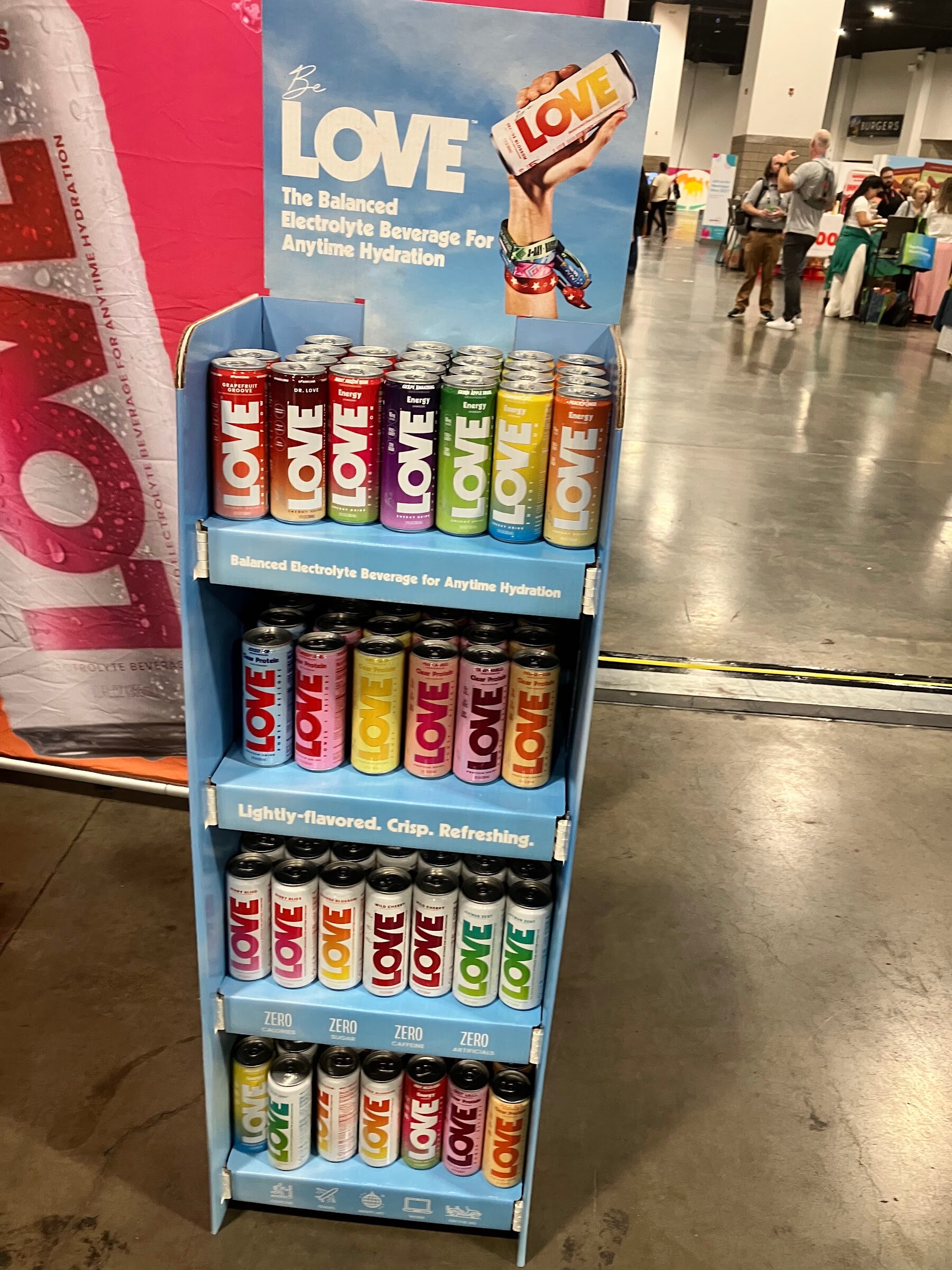 Blue cardboard floor display stocked with colorful cans of LOVE electrolyte drinks on the show floor.