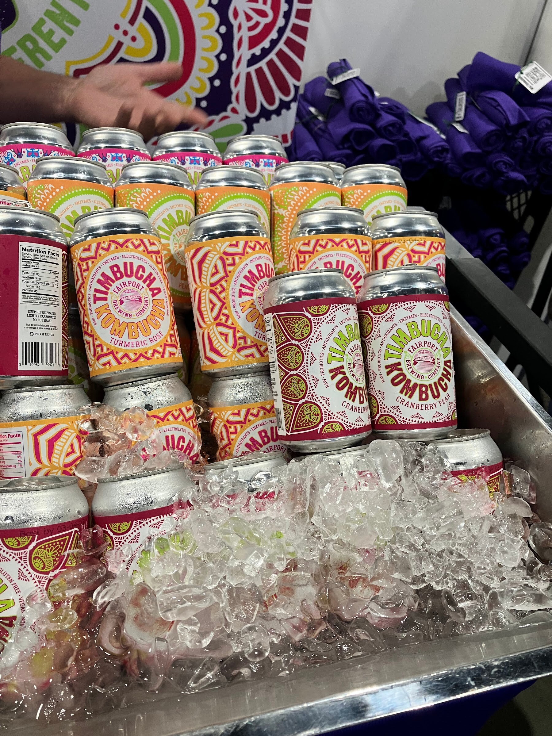 Cans of Timbucha kombucha with colorful patterned labels chilling on ice.