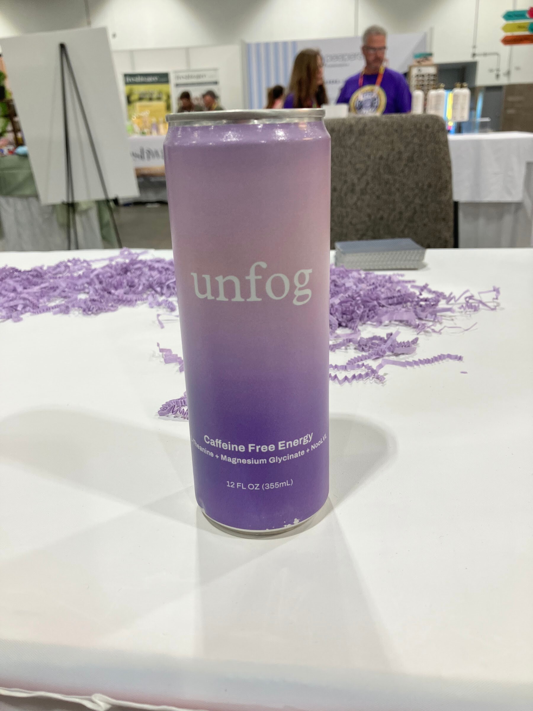 A lavender can of Unfog caffeine-free energy on a white table with purple shredded paper.