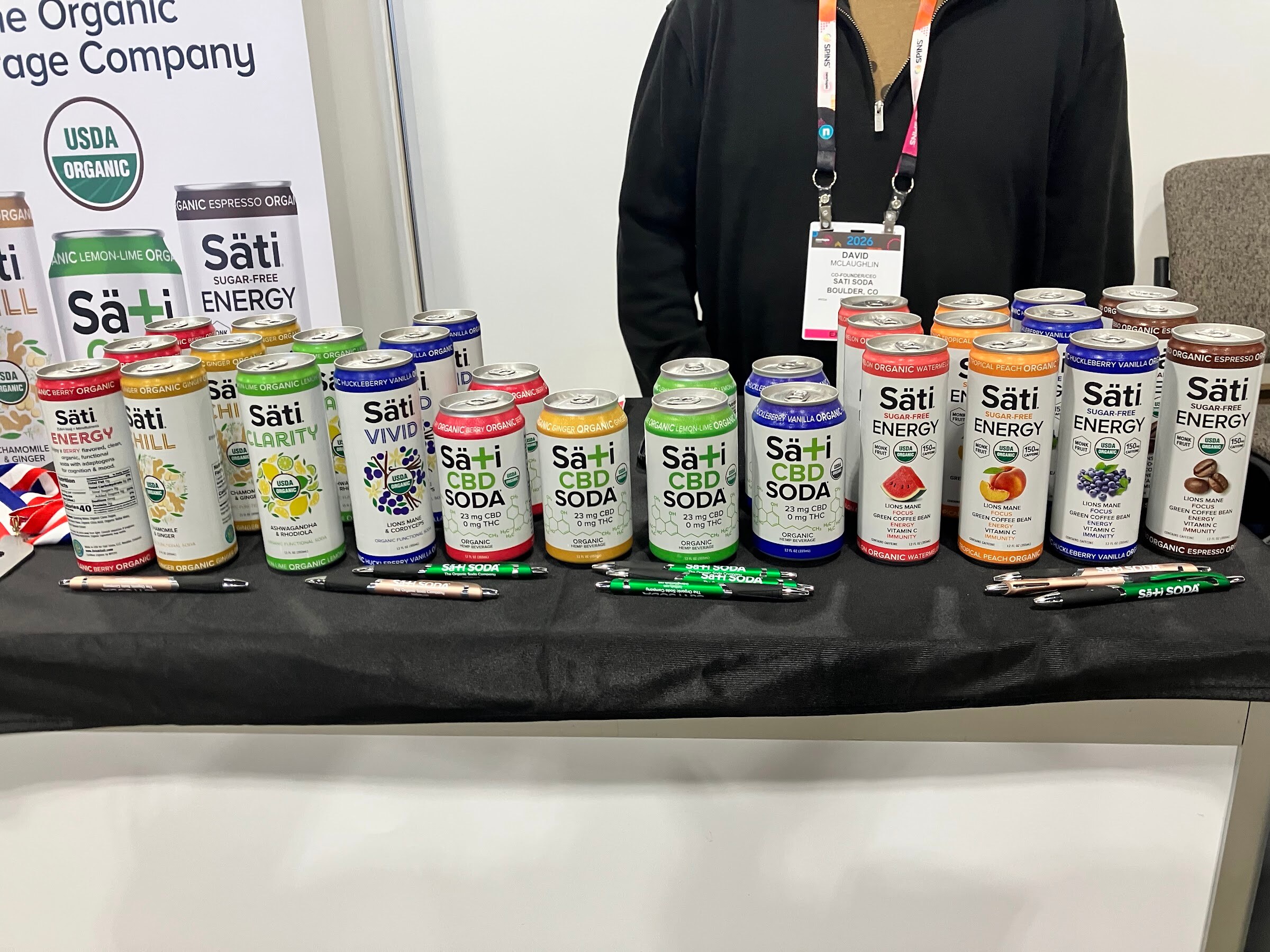 Rows of colorful Säti cans on a black tablecloth at the Säti Beverage Company booth.