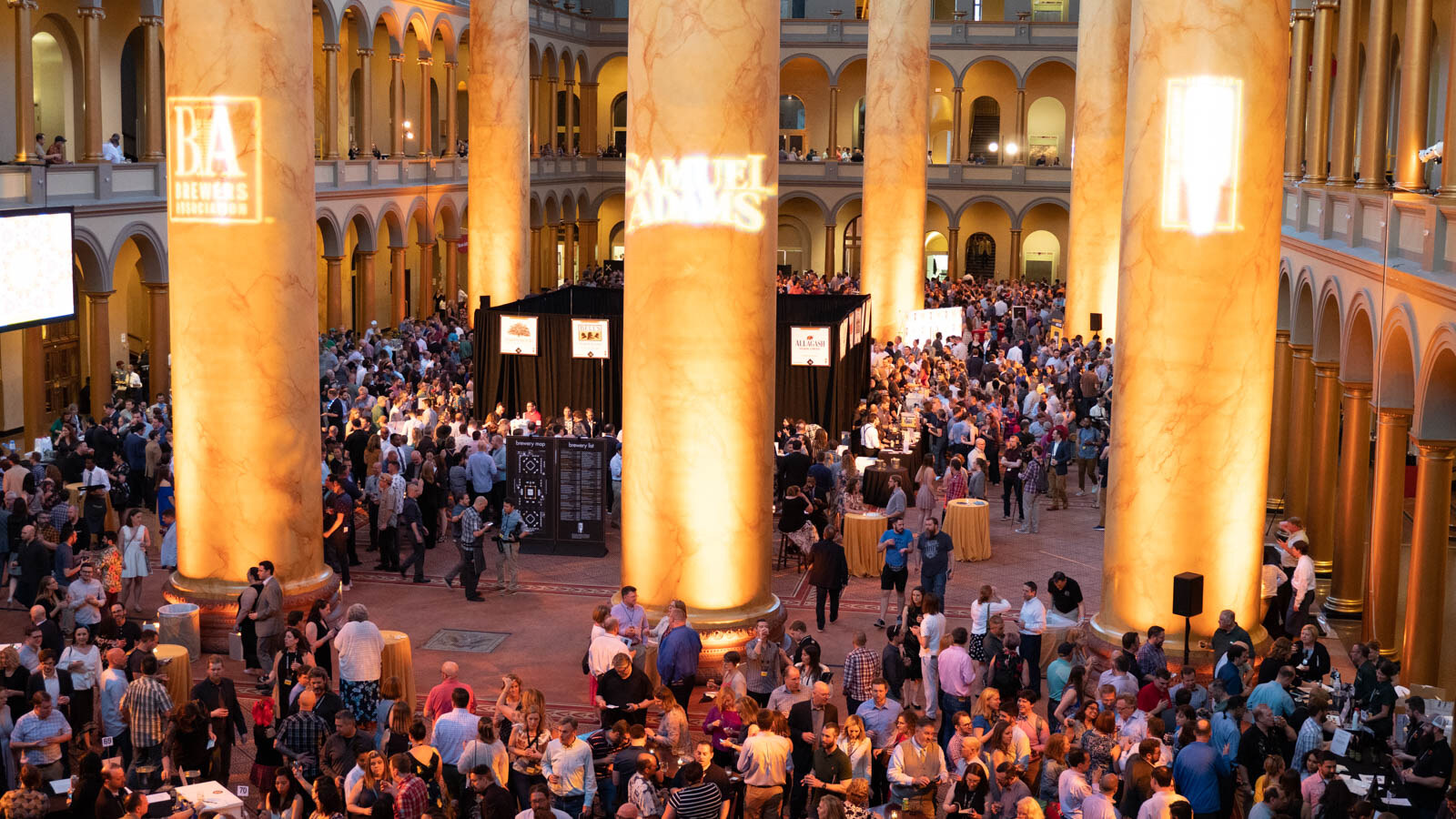 High view of a crowded hall with glowing columns carrying projected logos including Brewers Association and Samuel Adams.