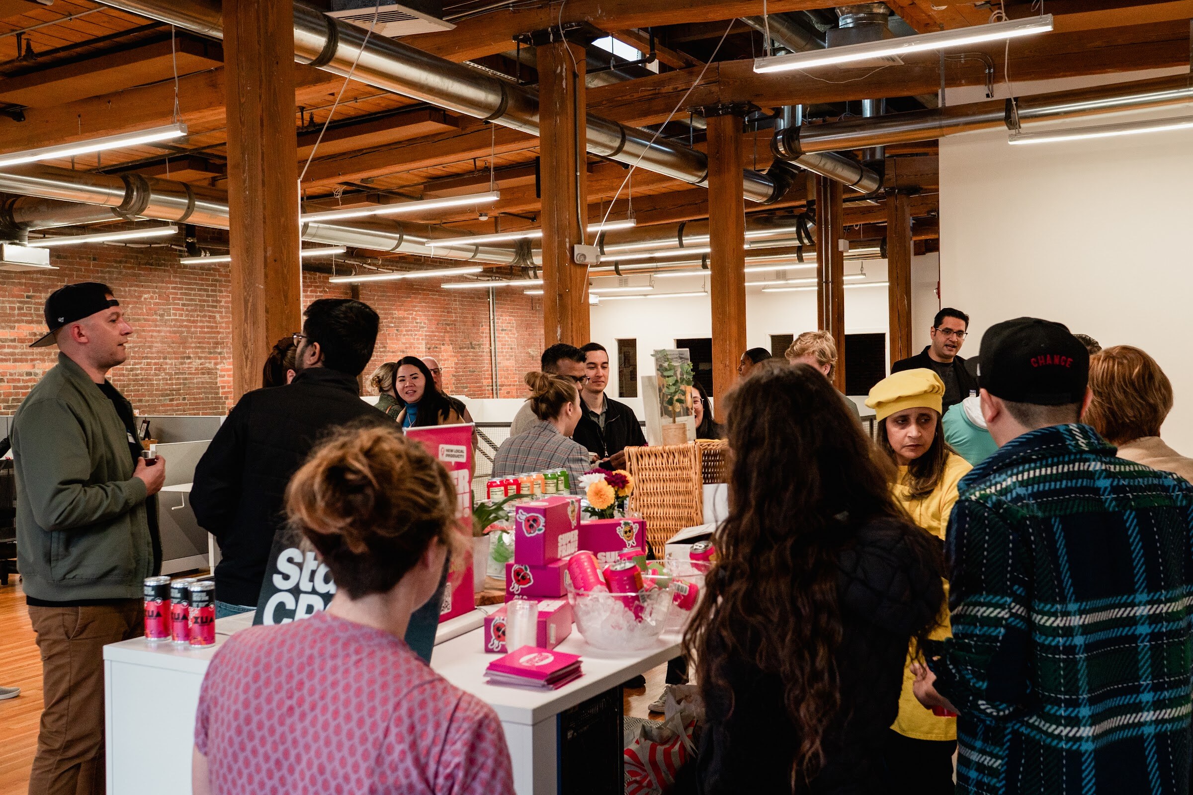 Guests crowd around a table with pink Super Frau boxes and cans, a Startup CPG sign and a wicker basket