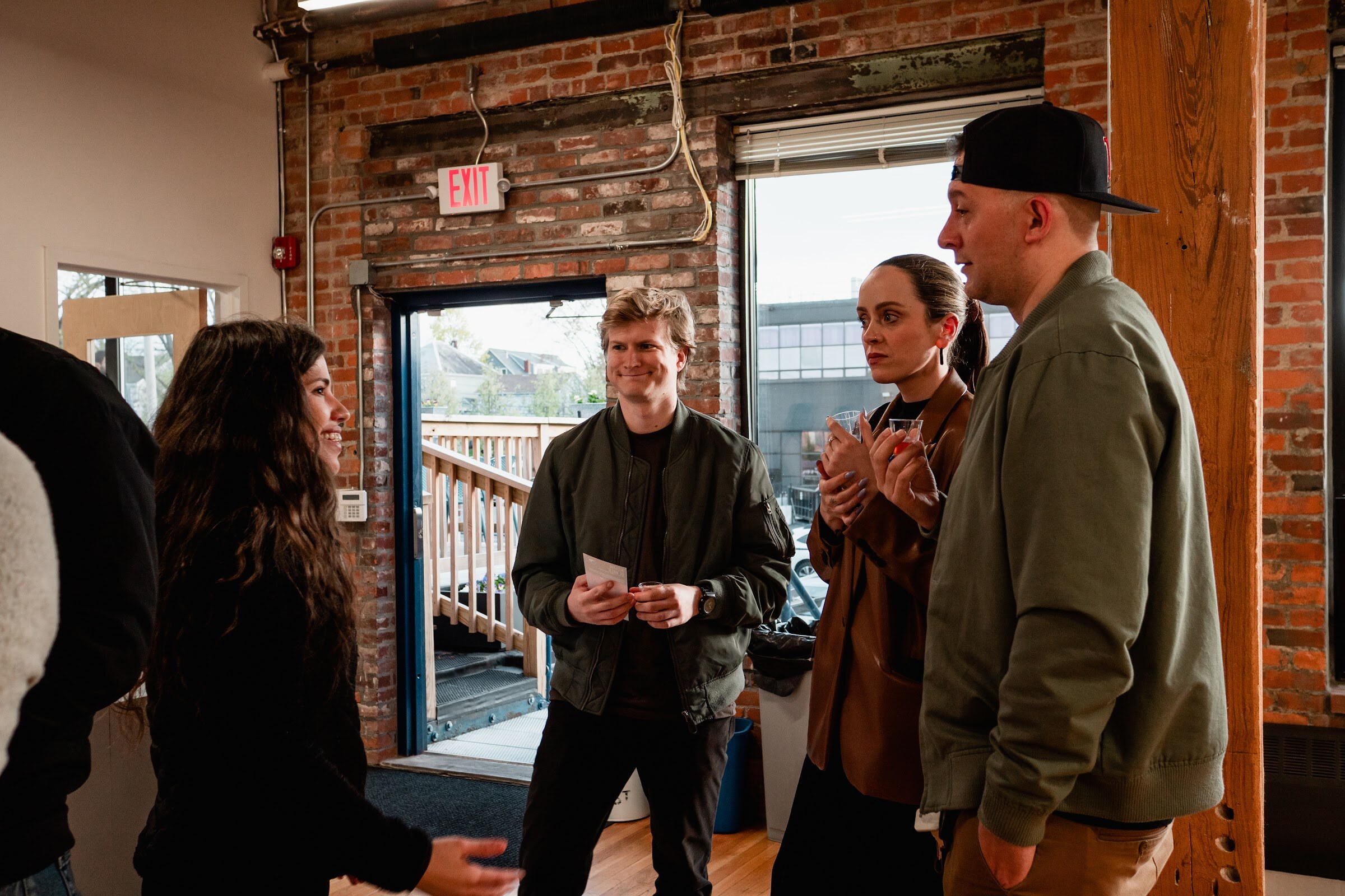 Three guests with drinks talk in a brick doorway that opens onto a wooden deck