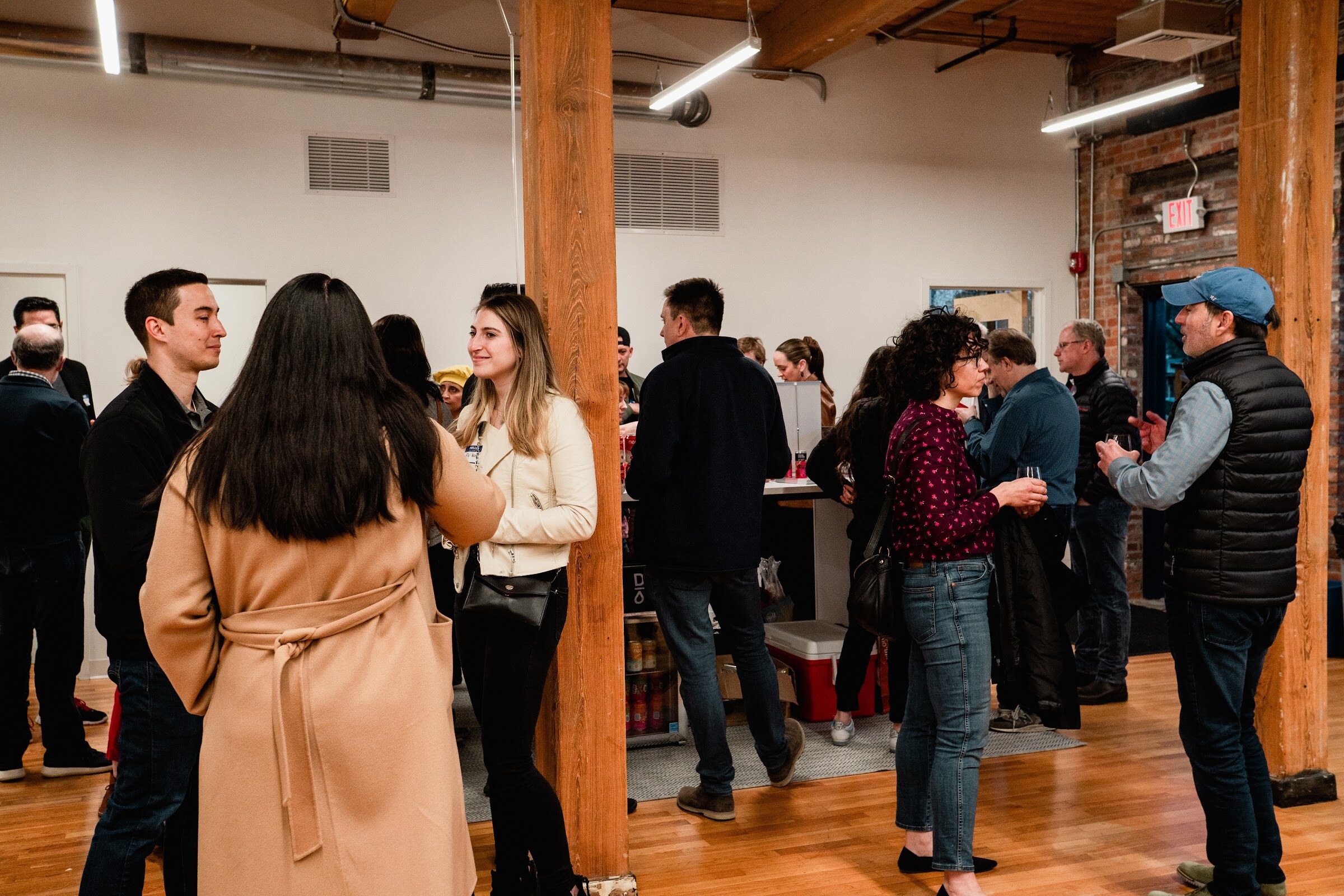 Attendees stand and talk in small groups under timber beams in a bright loft office