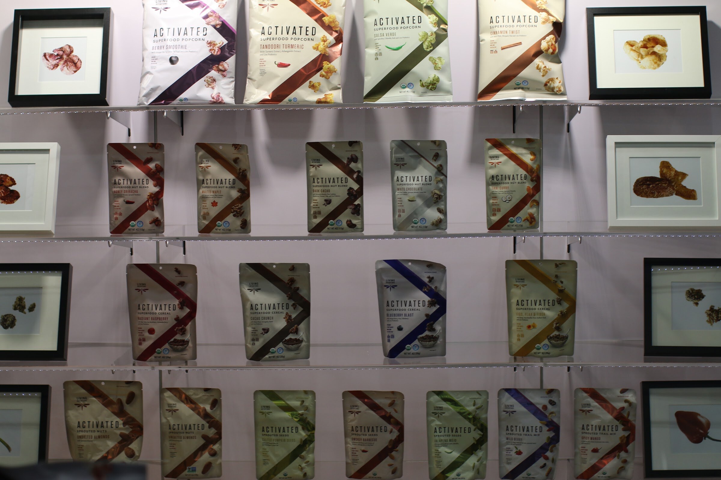 Shelves of Activated Living Intentions pouches in many flavors displayed on a lavender wall with framed photos.