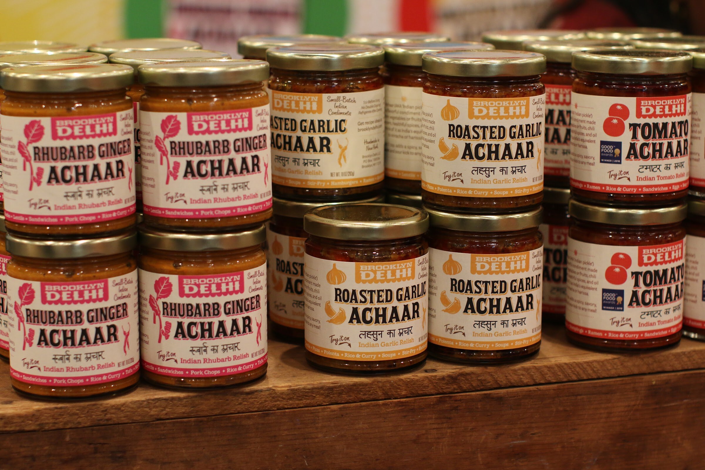 Stacks of Brooklyn Delhi Indian relish jars with colorful labels on a wooden display.