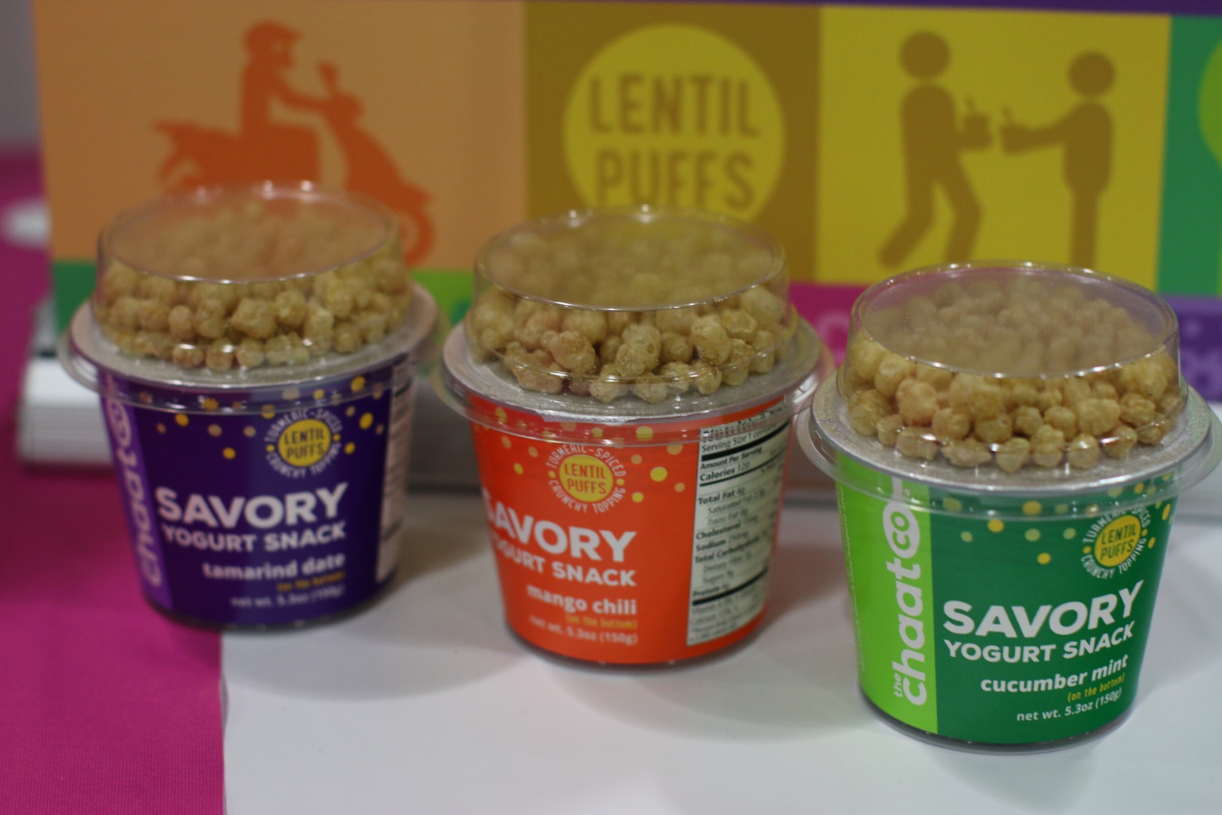 Three chaatCo savory yogurt snack cups, purple, orange and green, each topped with crunchy lentil puffs.