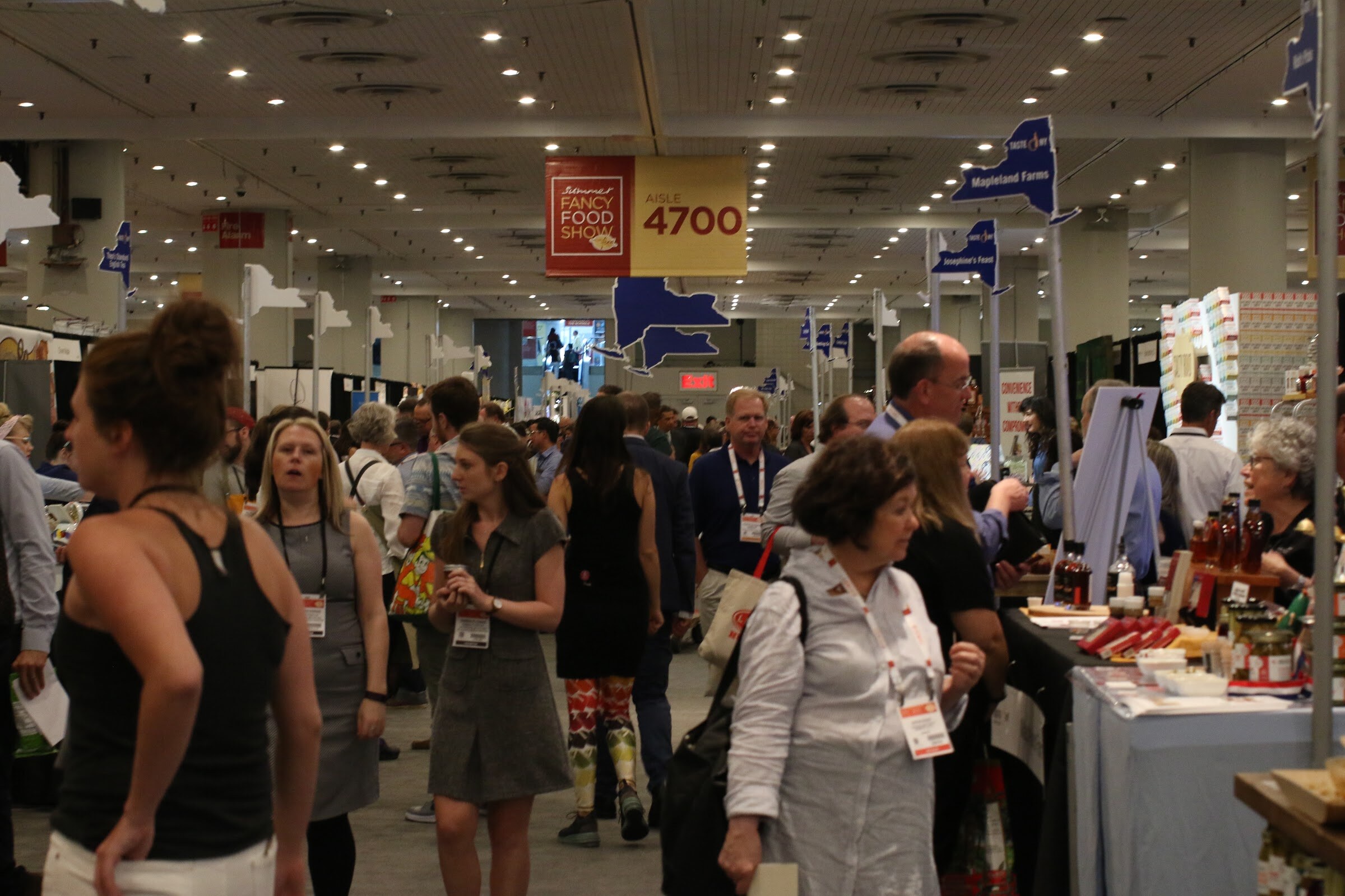 Crowd of badge-wearing attendees walking a trade show aisle under a Fancy Food Show sign marked Aisle 4700.