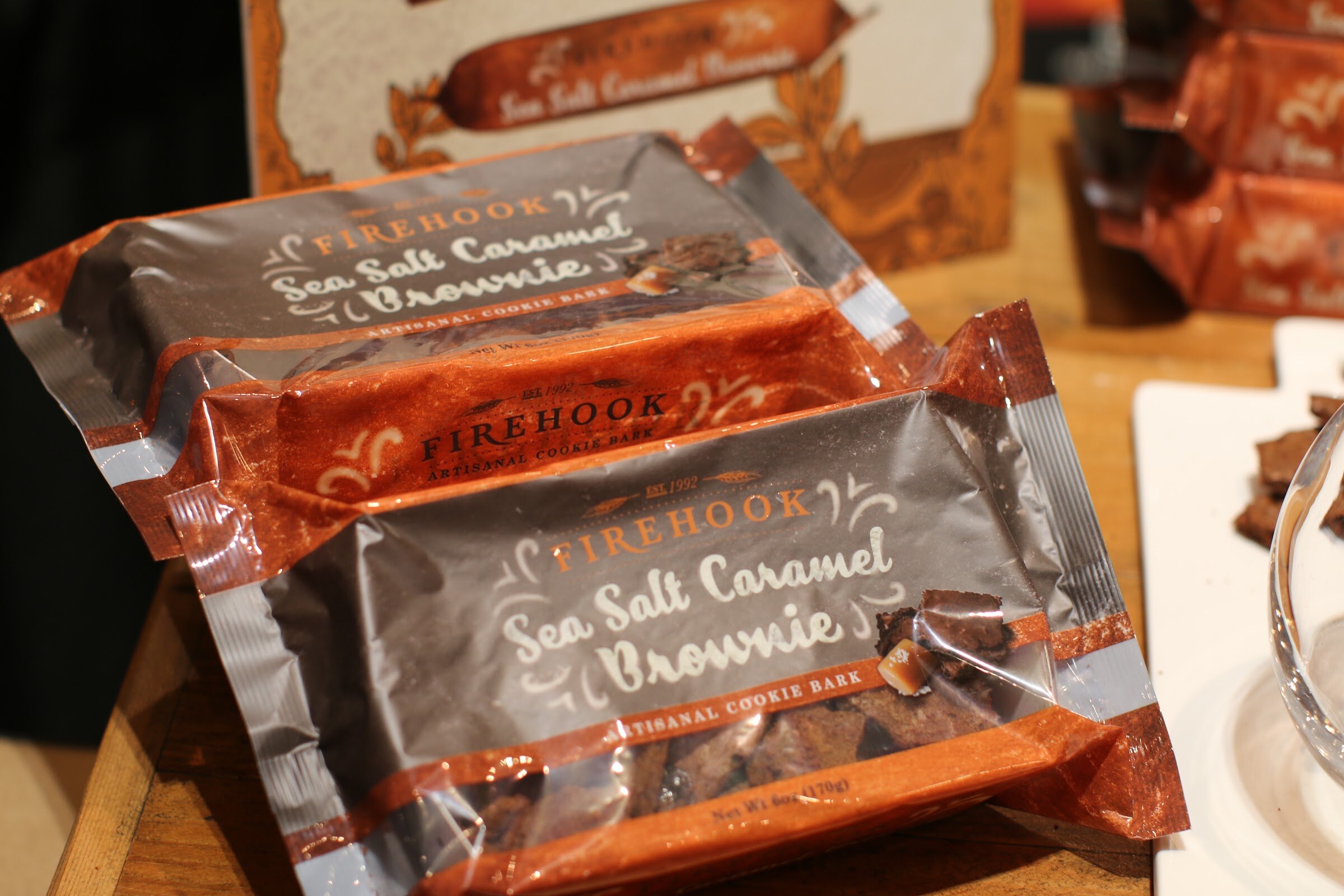 Two packages of Firehook sea salt caramel brownie cookie bark on a wooden table.