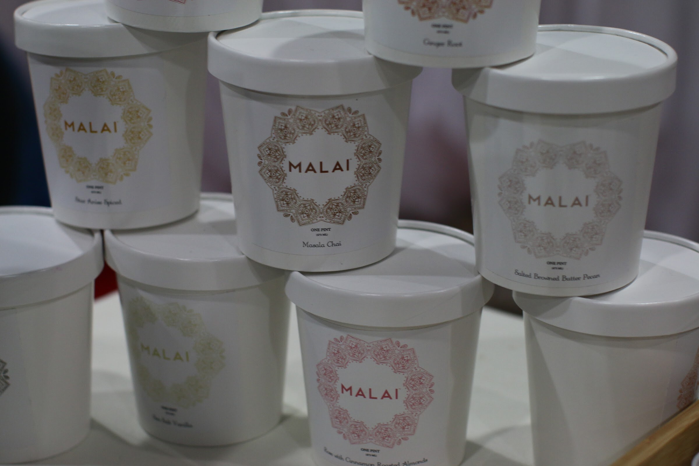 White Malai ice cream pint containers stacked in a pyramid with decorative circular labels.