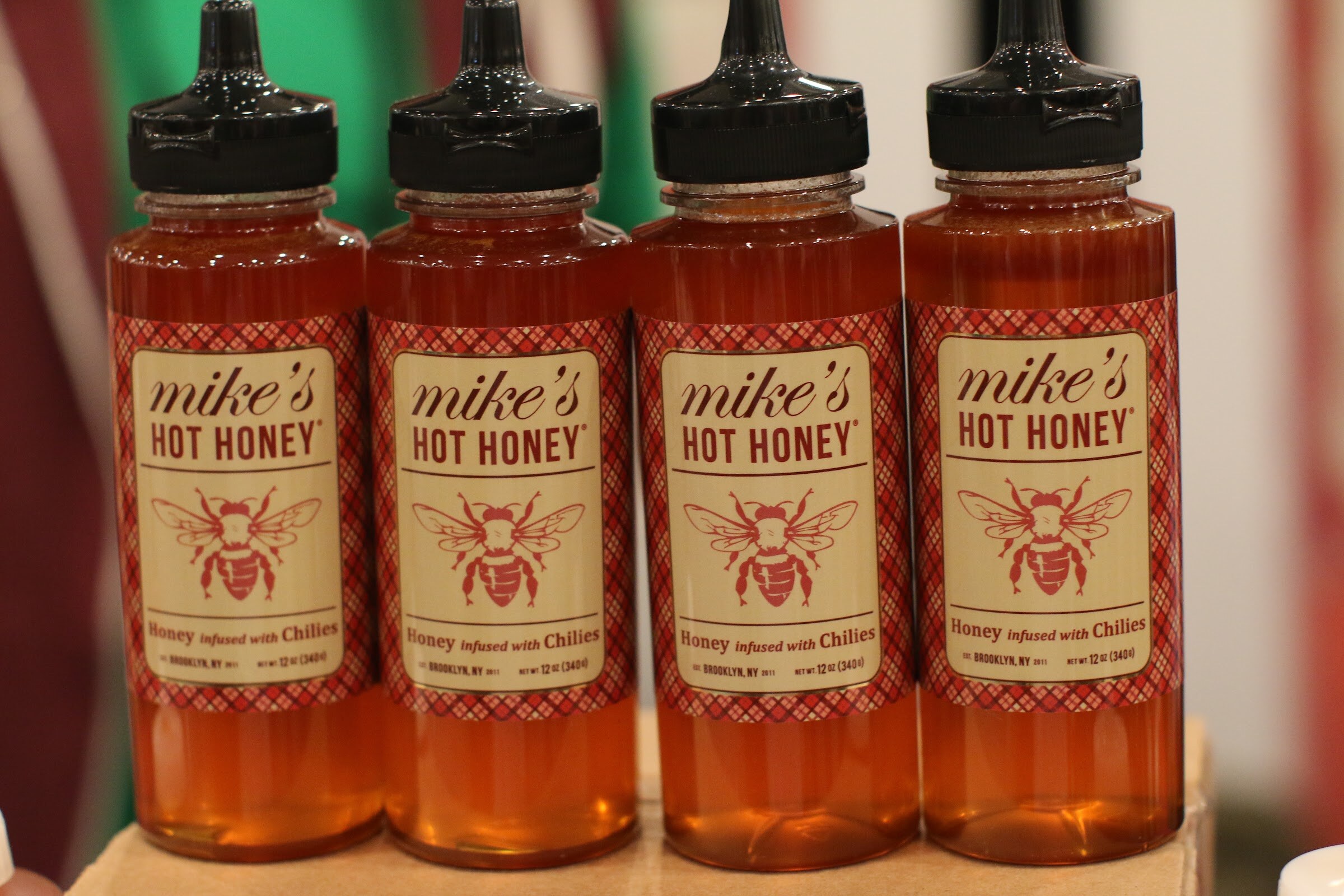Four identical bottles of Mike's Hot Honey with plaid red labels and black caps.