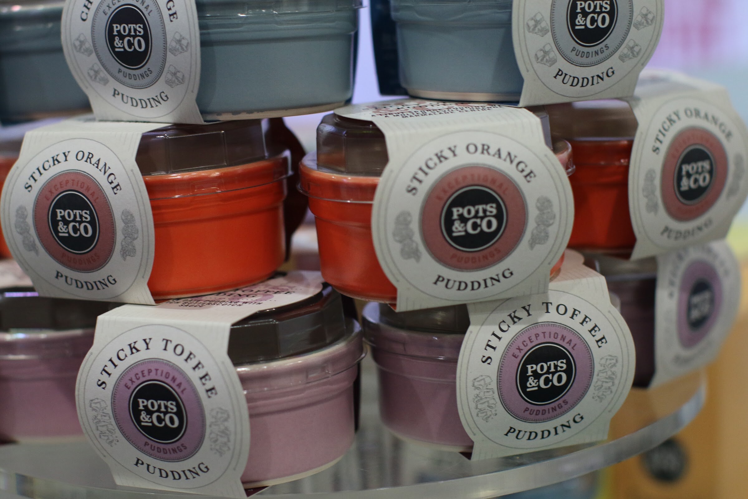 Stacks of small ceramic pudding pots with Pots and Co labels reading sticky orange and sticky toffee.