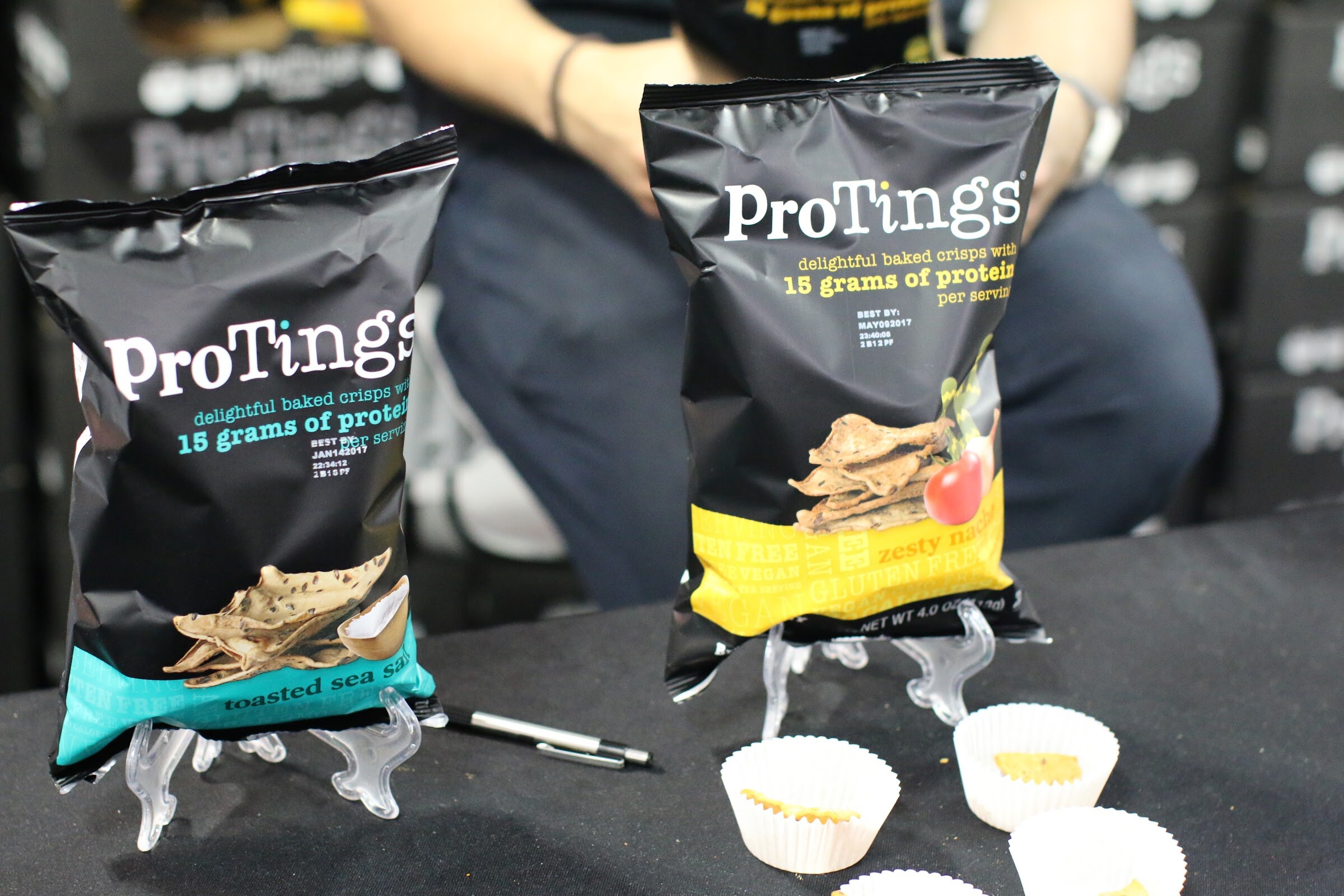Two black ProTings chip bags on clear stands with paper cups of samples on a black tablecloth.