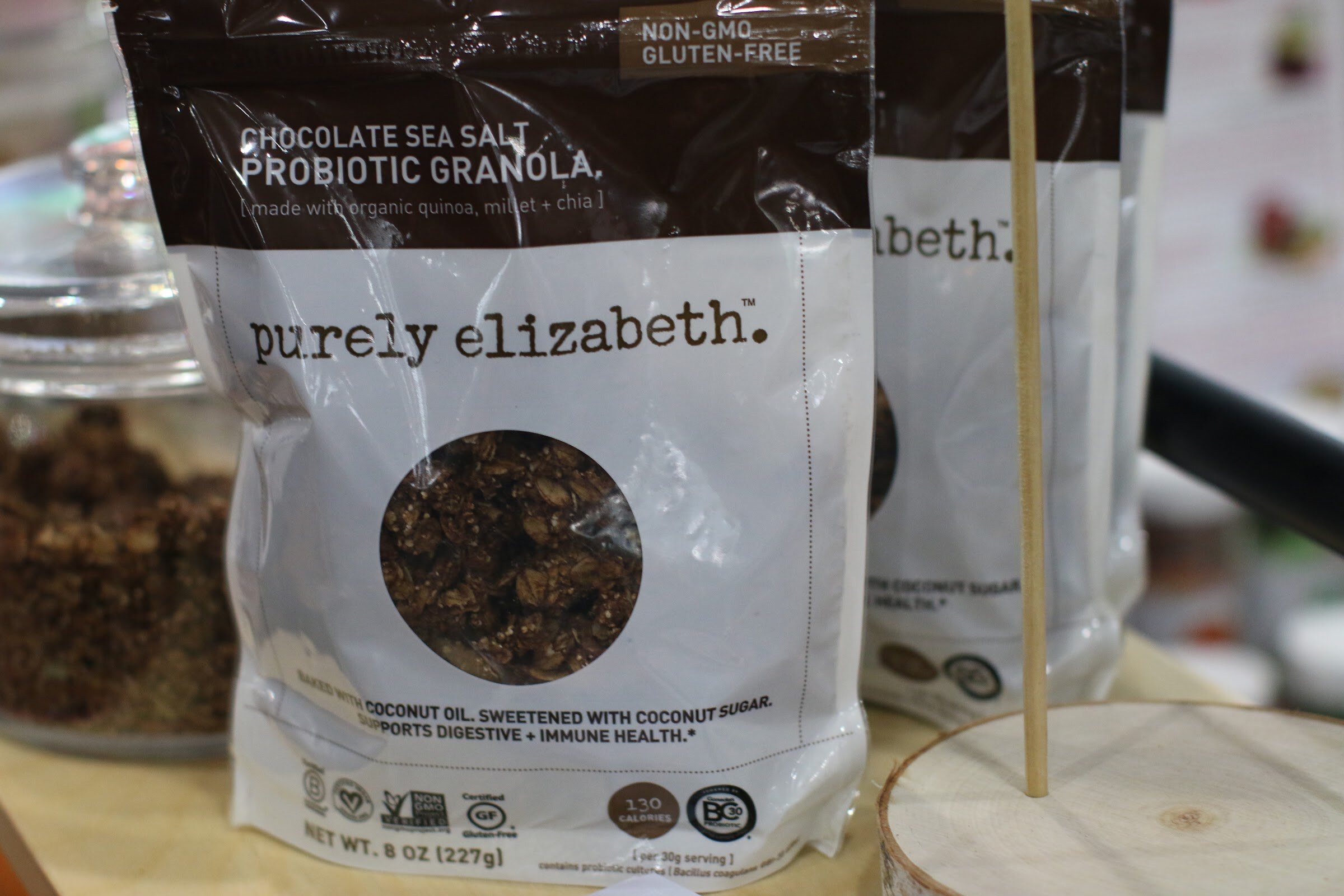 Close view of a purely elizabeth chocolate sea salt probiotic granola bag with a clear jar of granola behind it.