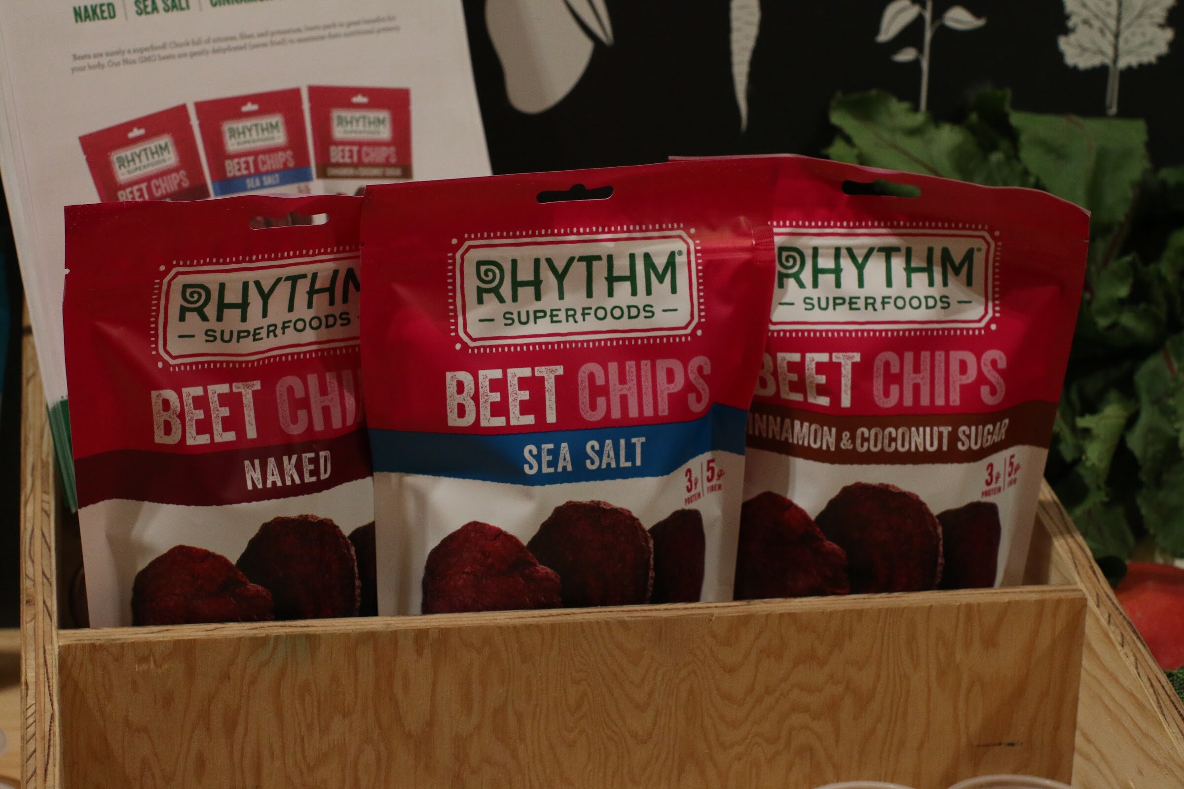 Three red bags of Rhythm Superfoods beet chips standing in a plywood crate.