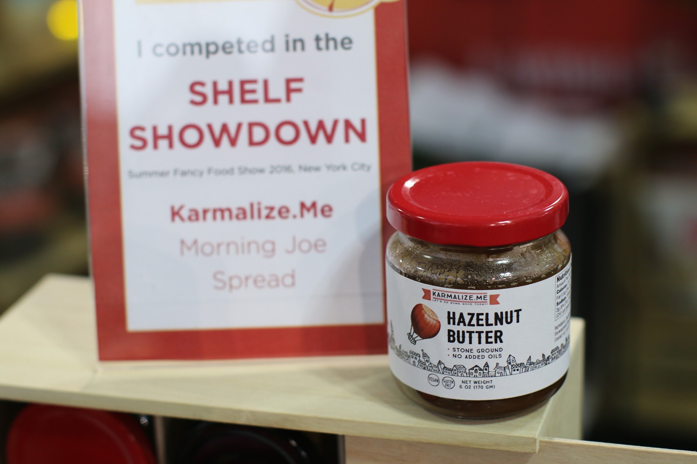 Red and white sign reading I competed in the Shelf Showdown beside a jar of Karmalize.Me hazelnut butter with a red lid.