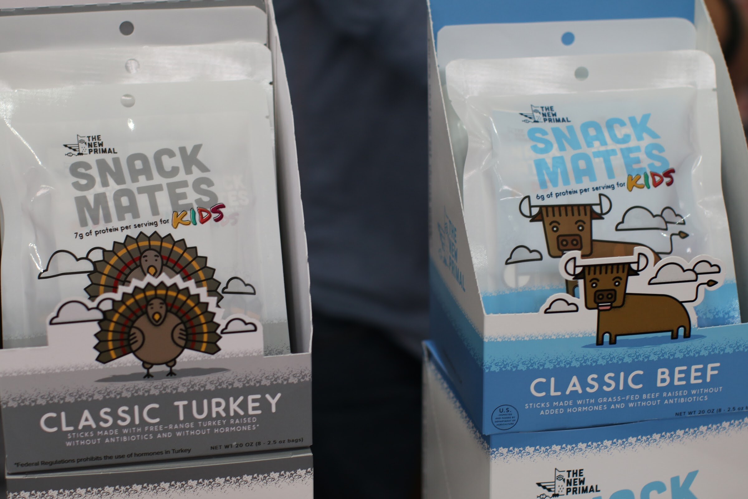 Two open display boxes of Snack Mates pouches with cartoon turkey and bison characters.