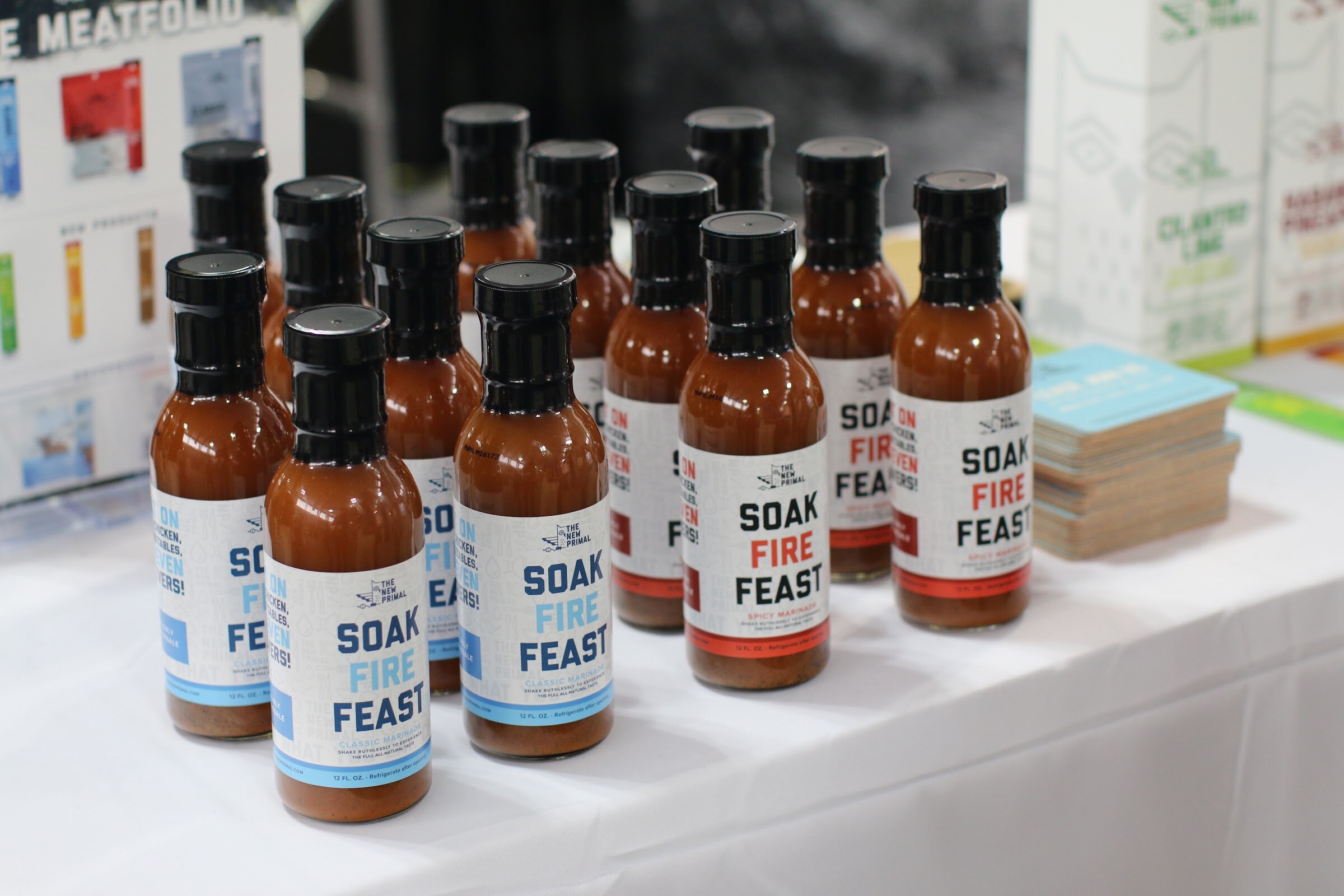 Two groups of brown sauce bottles with Soak Fire Feast labels on a table with a white tablecloth.