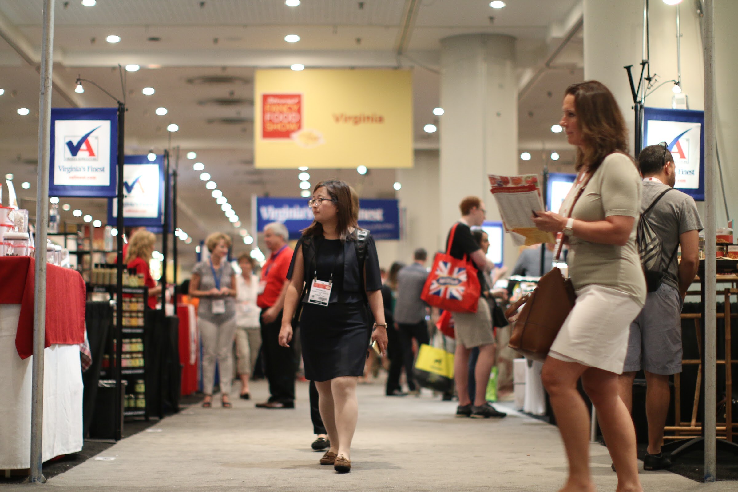 Woman with a badge walking down an exhibit aisle under a yellow Virginia sign, with Virginia's Finest signs on both sides.
