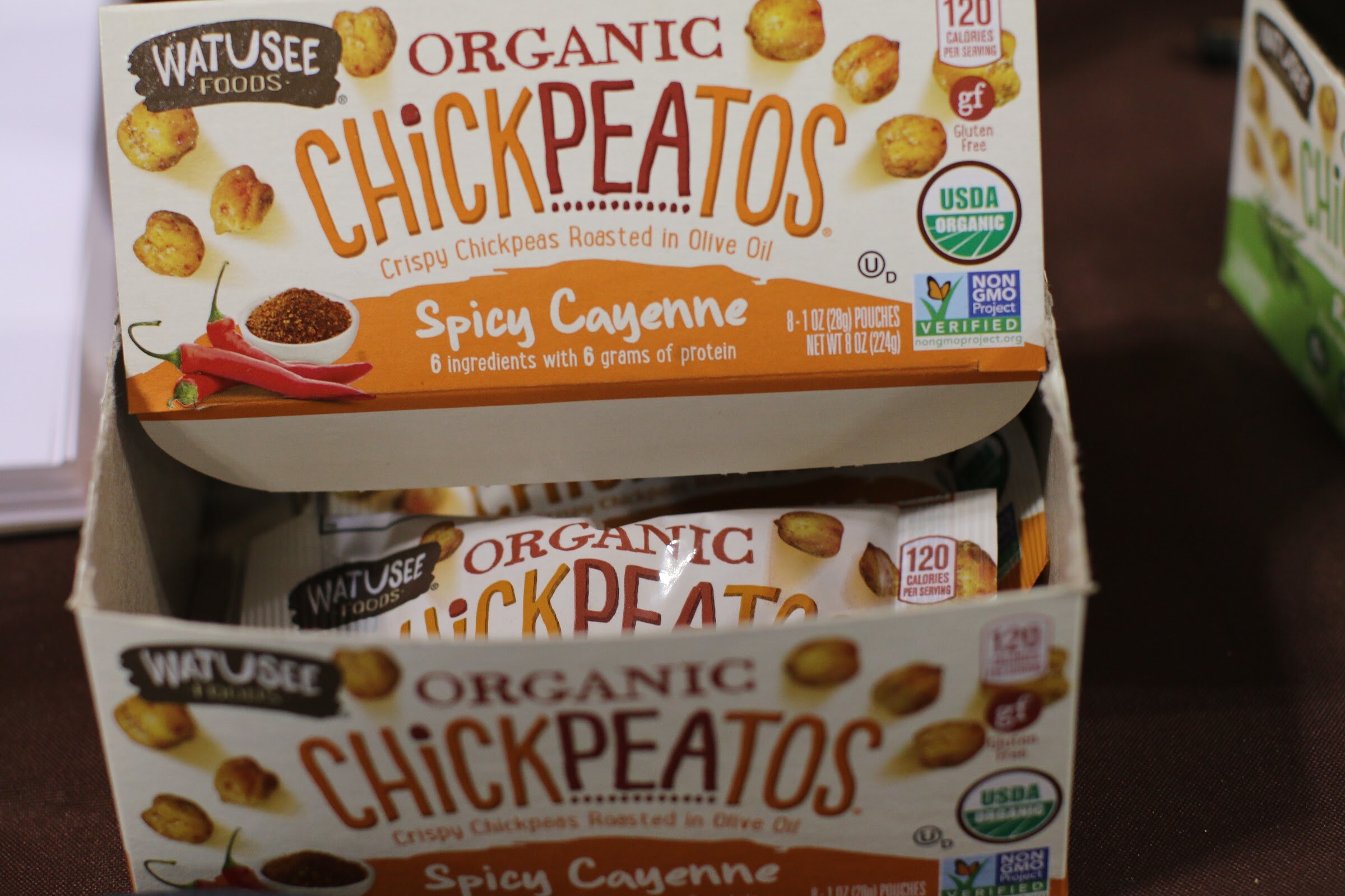 Open cardboard display box of Watusee Foods Organic Chickpeatos spicy cayenne snack pouches.