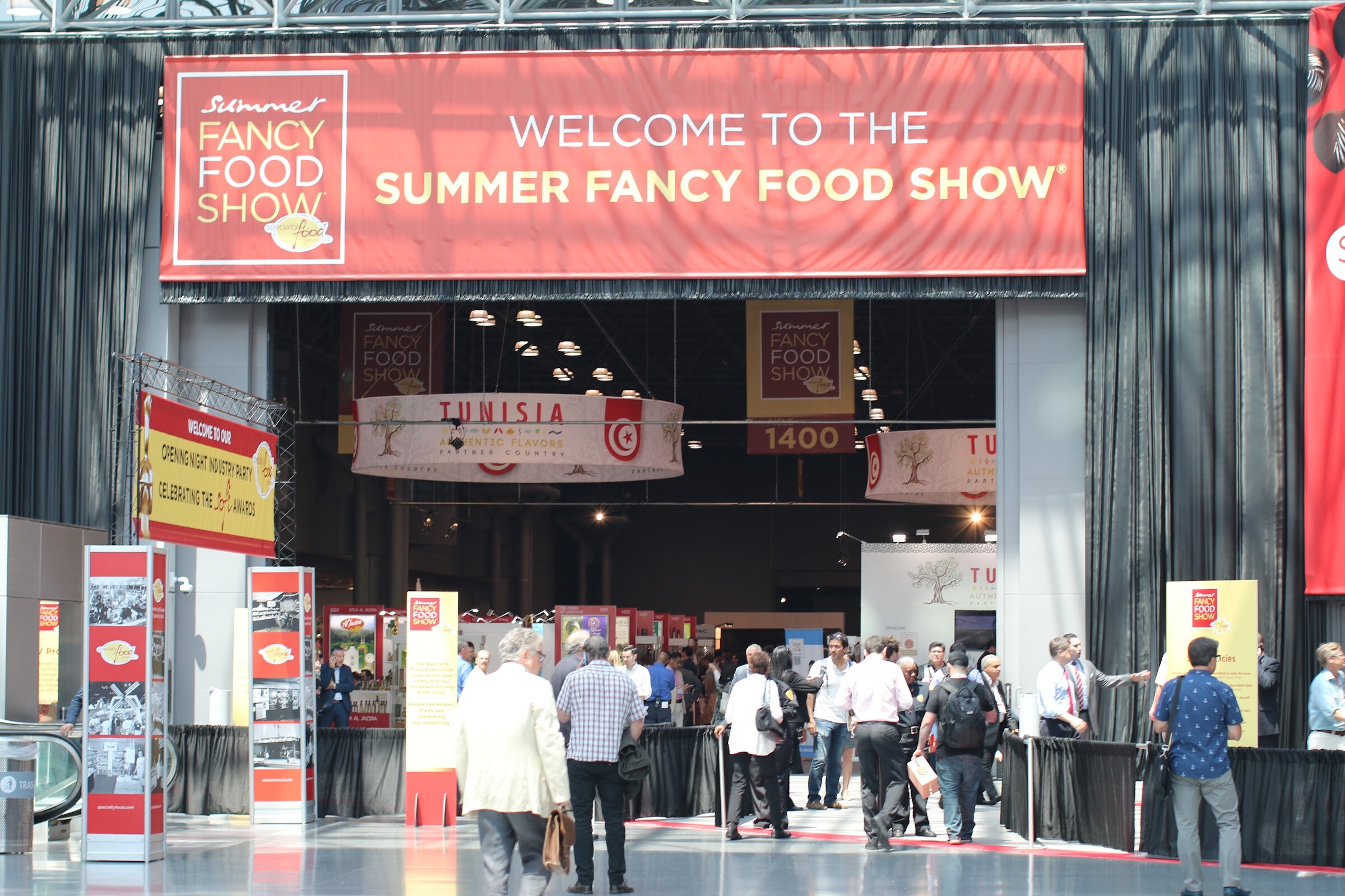 Large red banner reading Welcome to the Summer Fancy Food Show above an entrance with attendees heading inside.
