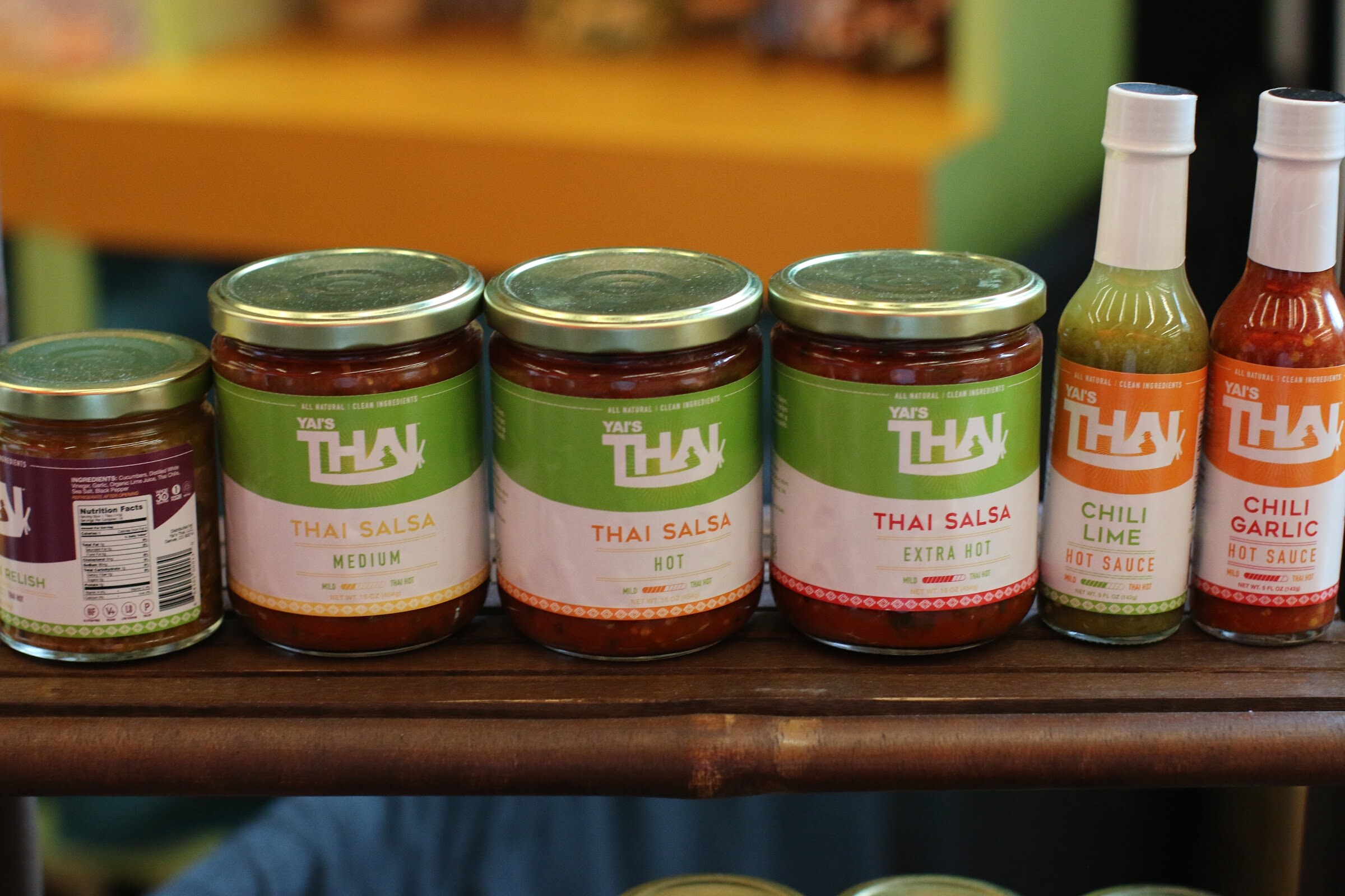 Row of jars and bottles of Yai's Thai salsas and hot sauces on a wooden shelf.