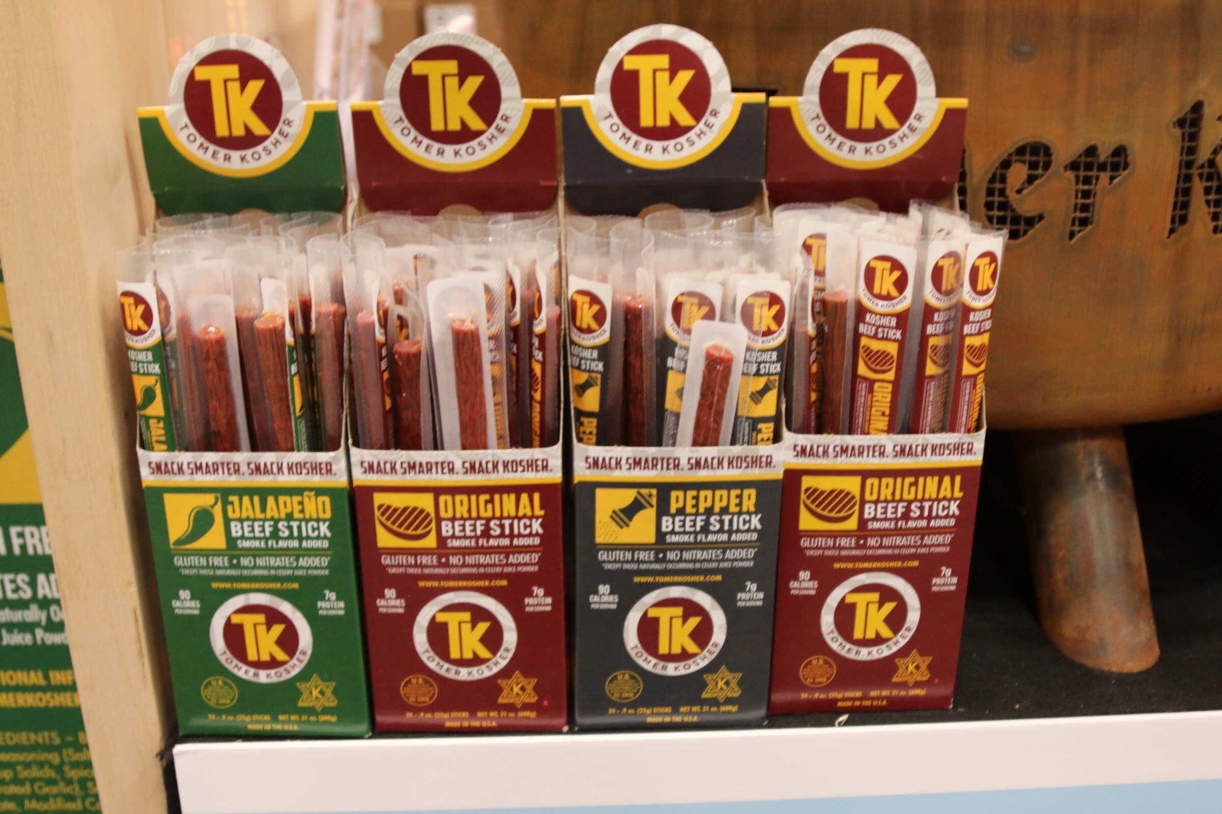 Several display boxes of Tomer Kosher beef sticks in green, maroon and black packaging on a shelf.