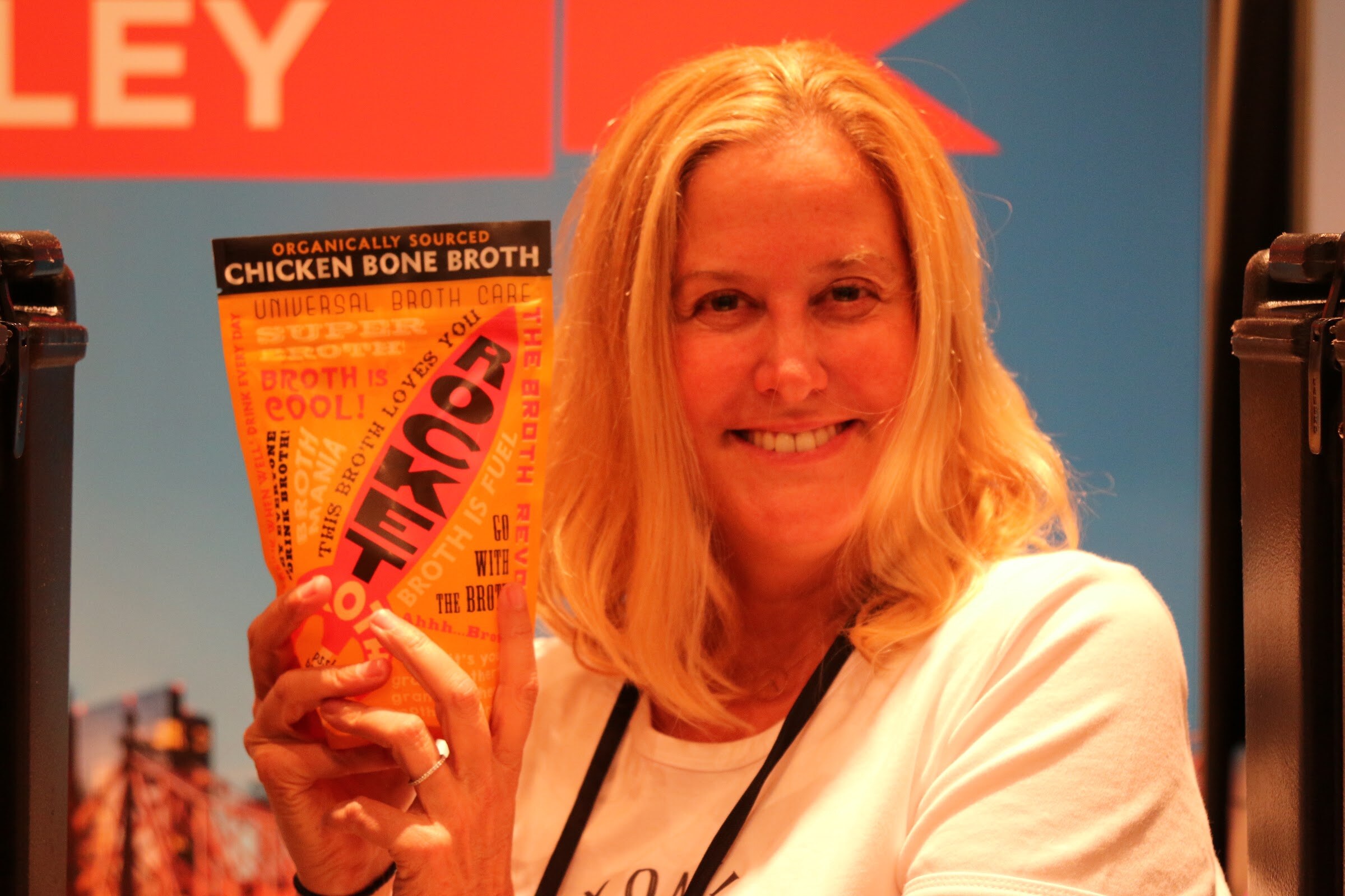 A smiling woman with blonde hair holding an orange Rocket chicken bone broth pouch.