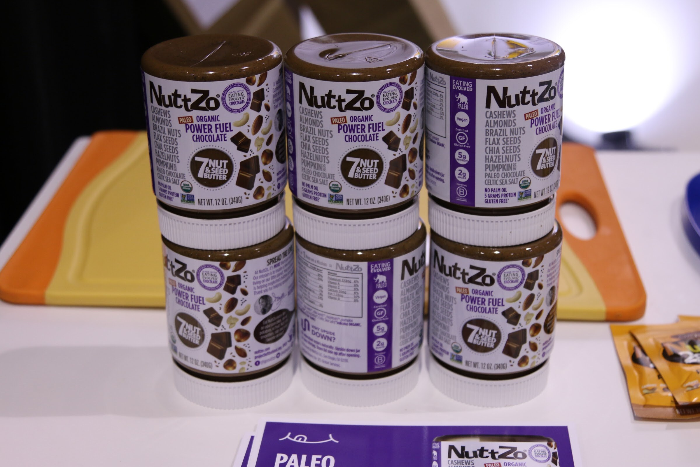 Two stacks of NuttZo Power Fuel Chocolate jars with purple labels on a white table.