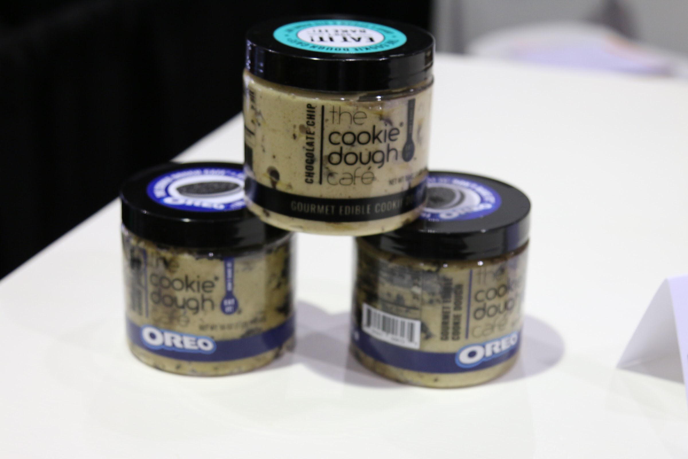 Three stacked jars of edible cookie dough with black lids and Oreo branding on a white table.