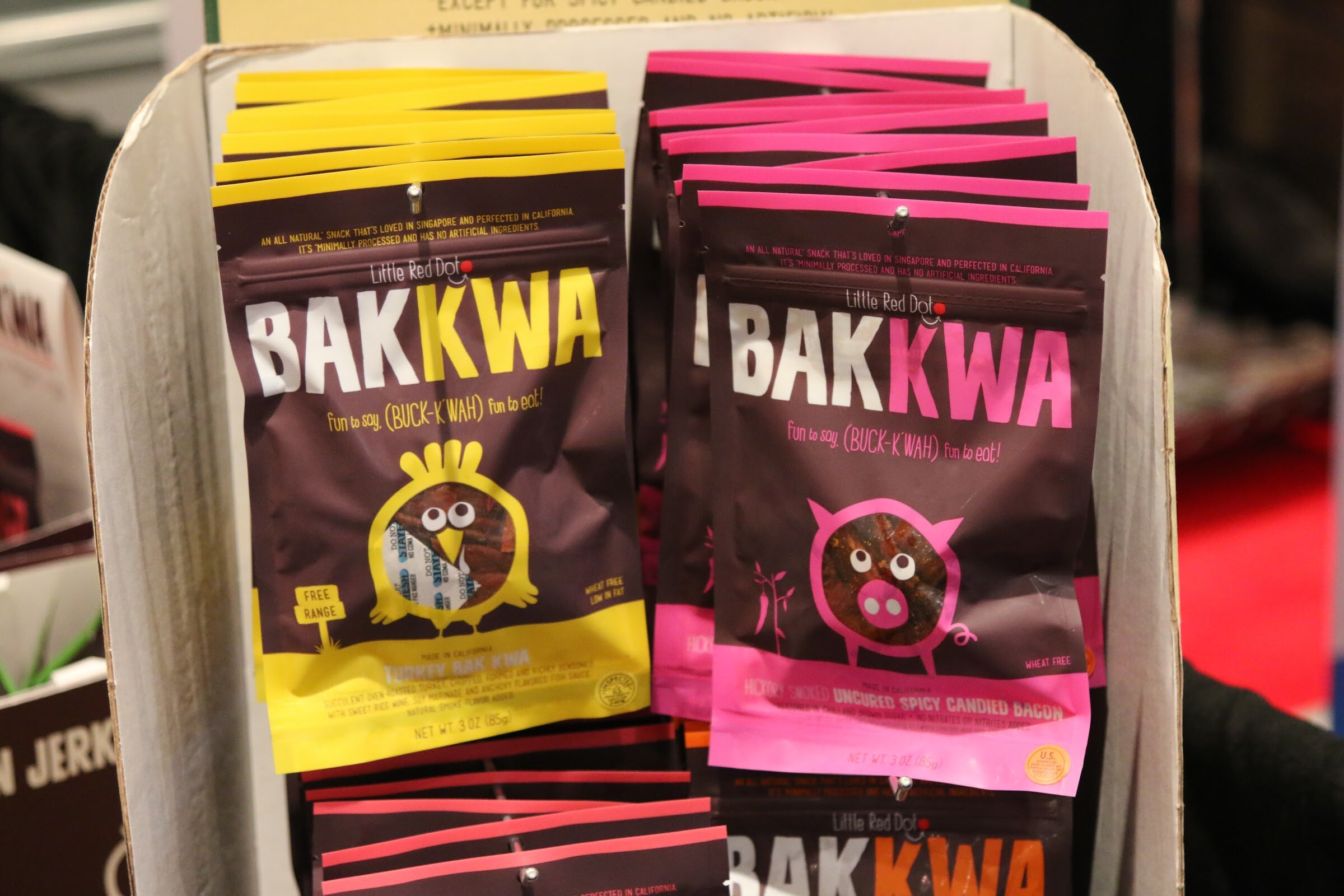 Yellow and pink bags of Little Red Dot Bakkwa jerky in a cardboard display.