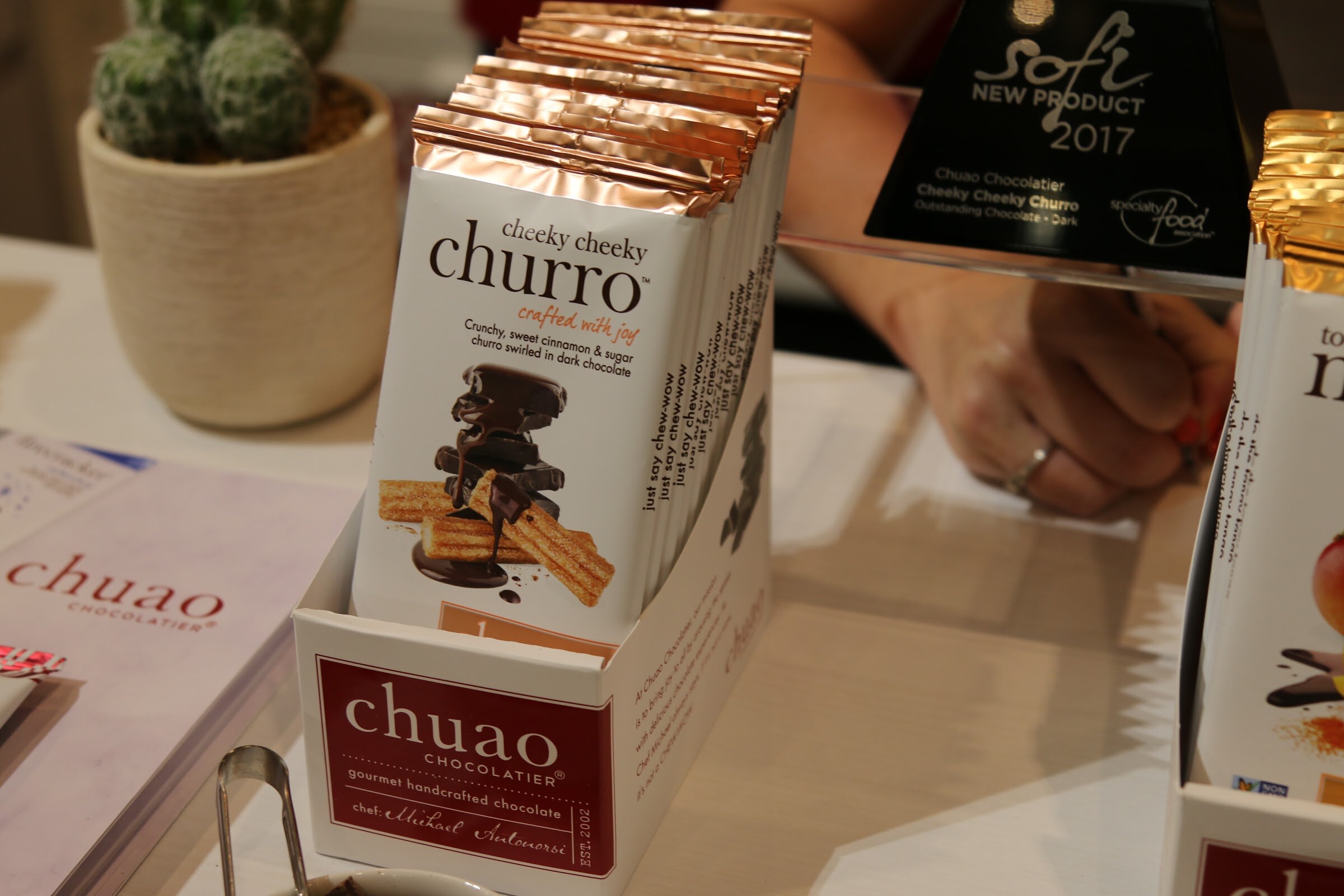 A white and copper chocolate bar box labeled chuao Cheeky Cheeky Churro next to a black sofi New Product award.