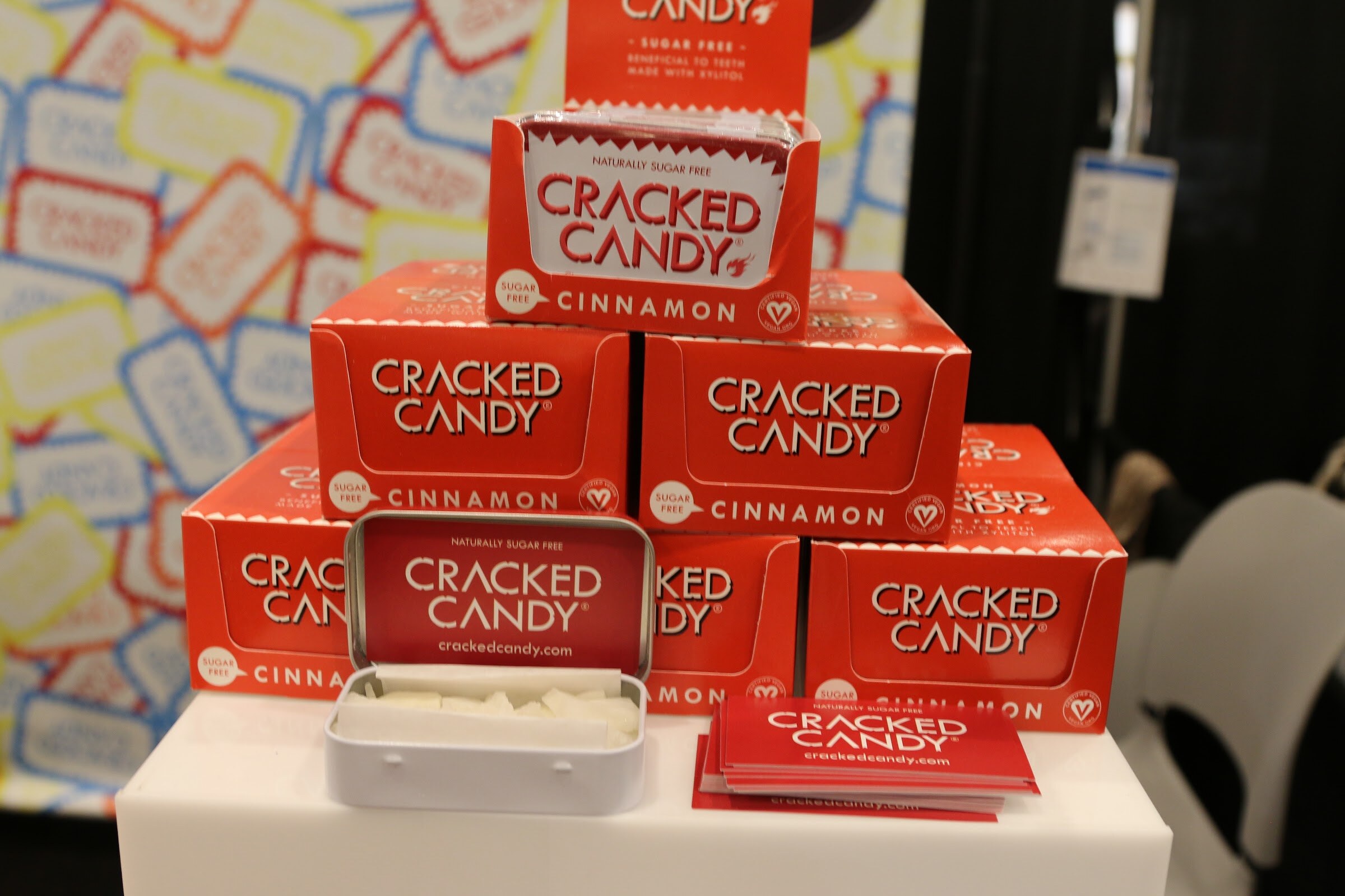 A pyramid of red Cracked Candy cinnamon boxes with an open tin of candy and business cards.