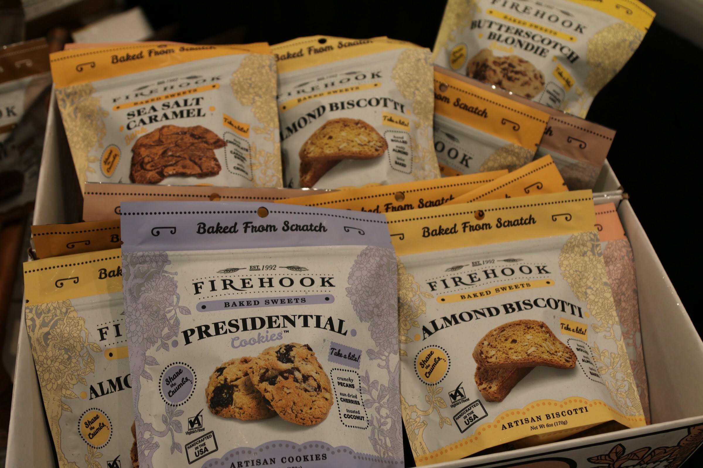 Several bags of Firehook baked sweets in lavender and yellow packaging in a bin.