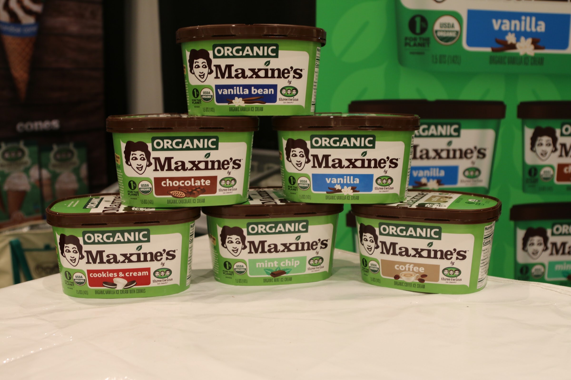 Green containers of Organic Maxine's ice cream stacked in a pyramid in front of a green backdrop.
