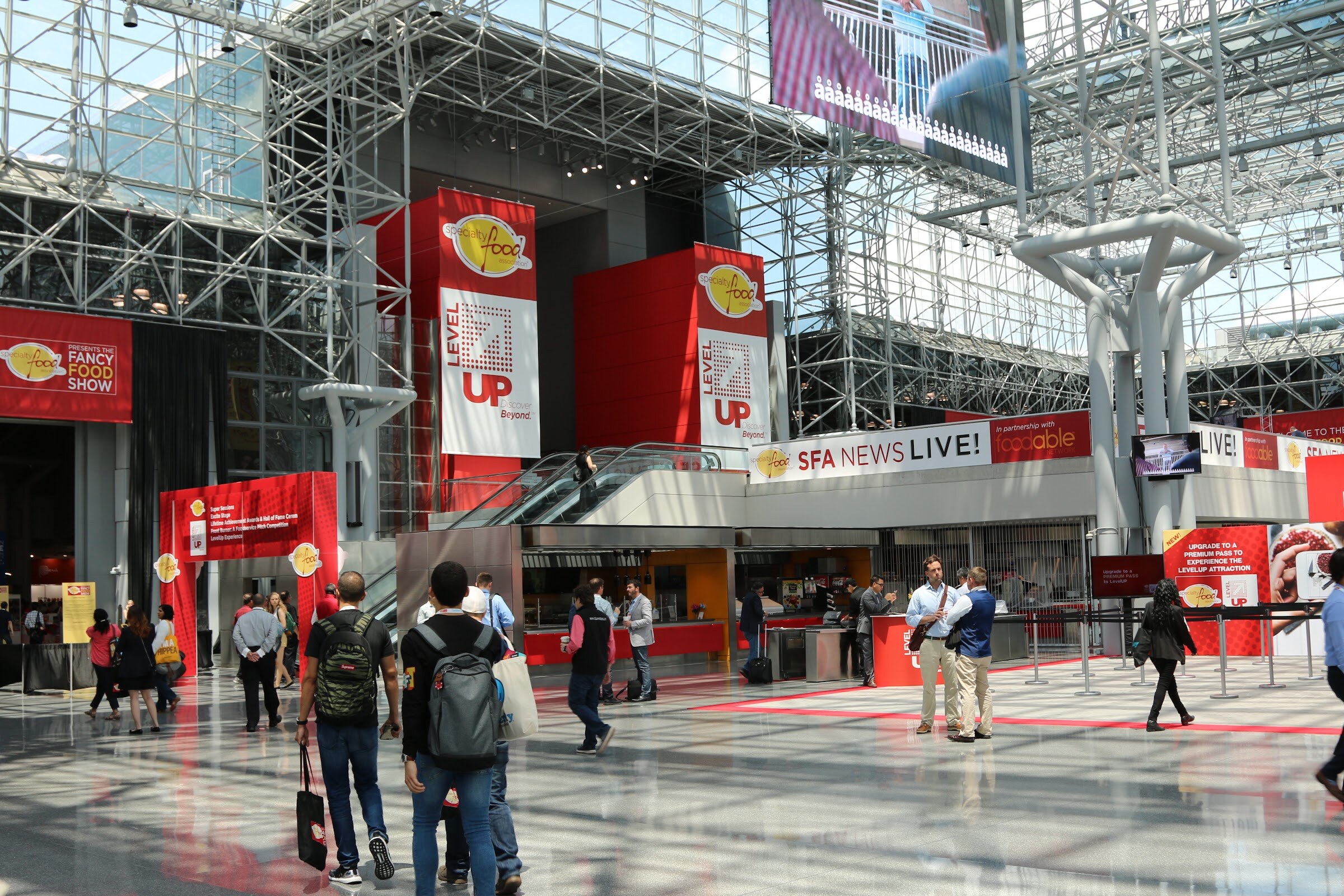 A wide glass-roofed lobby with red Level Up banners, an SFA News Live sign and a few dozen people.
